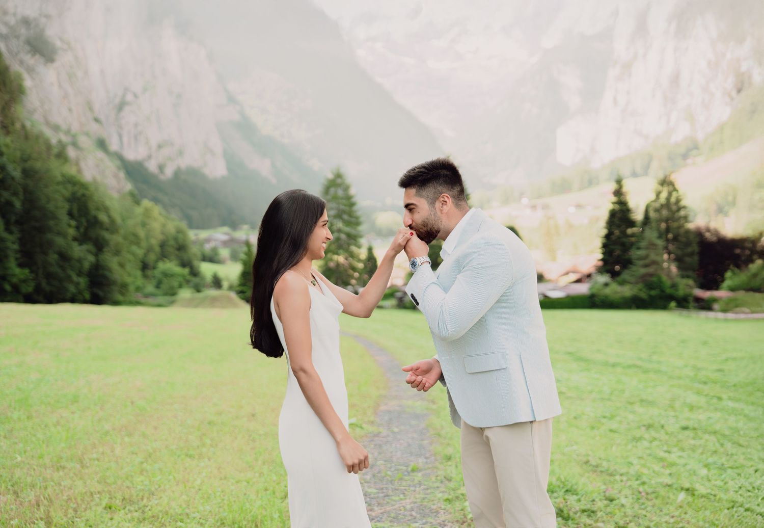 Groom kissing bride's hand during romantic proposal in scenic Lauterbrunnen valley, Switzerland.