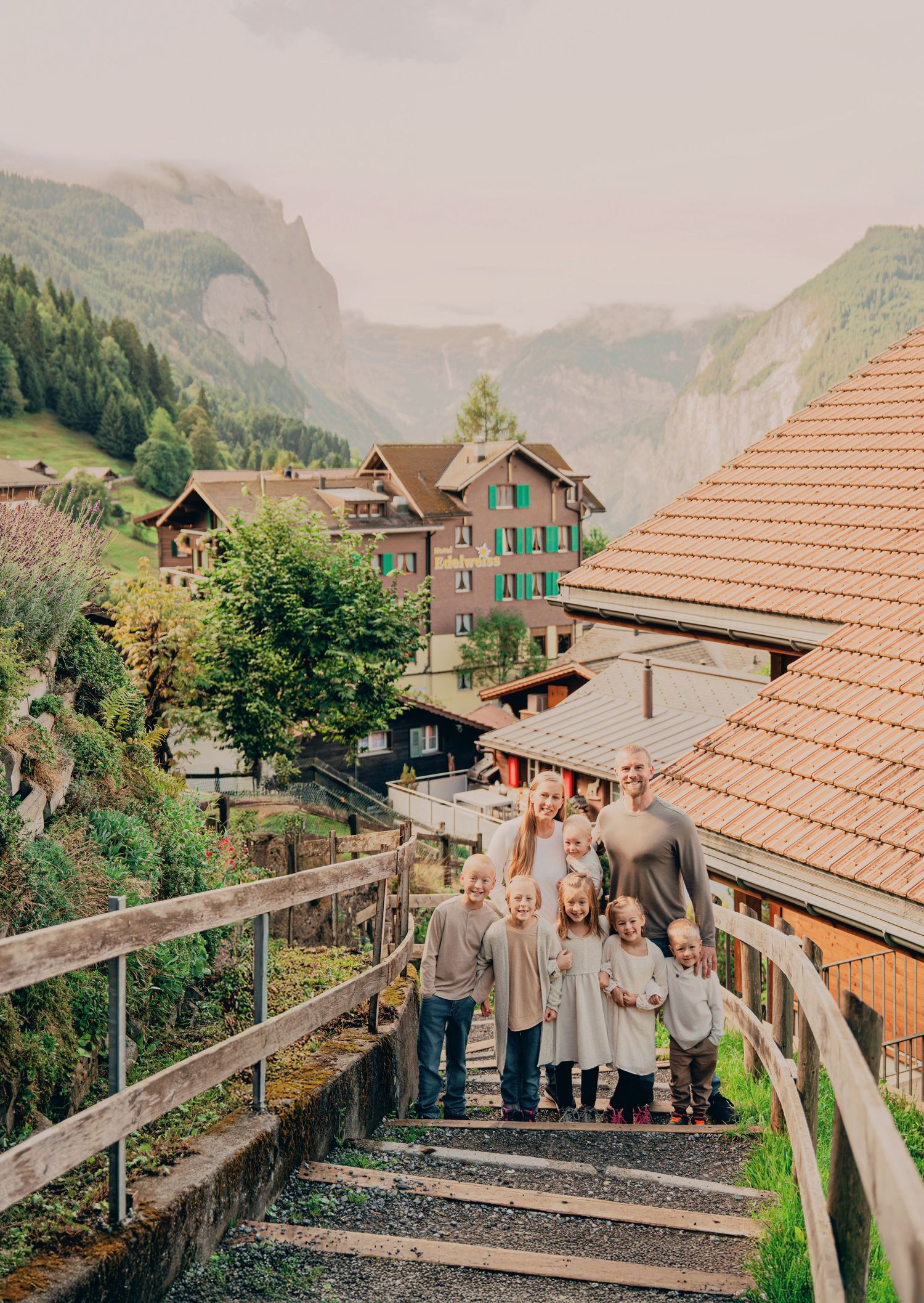 A large family of eight poses on stone steps in a picturesque Swiss alpine mountain village.