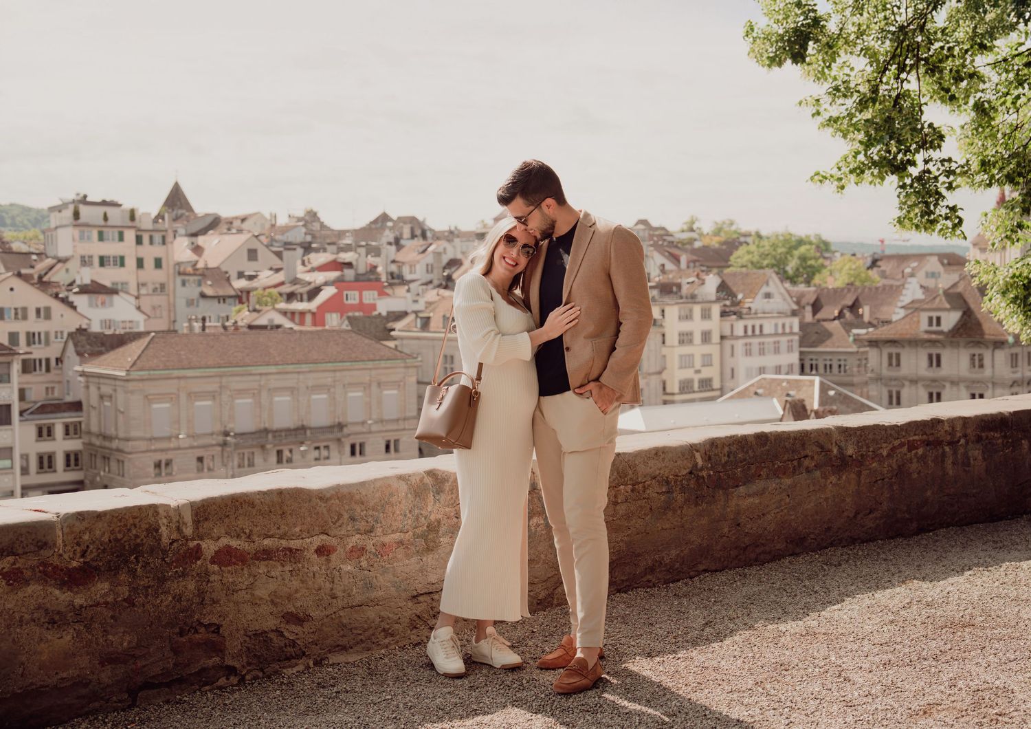 Couple shares tender moment on Zurich old town terrace wall with panoramic cityscape rooftops behind them.