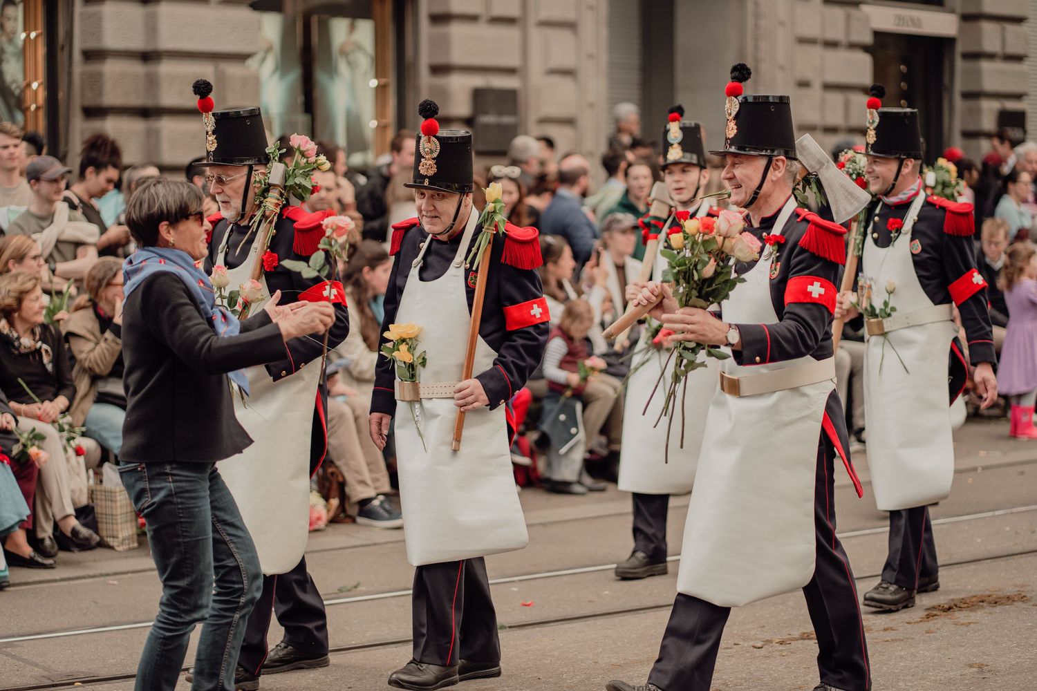 Performers in black and white historical costumes distribute flowers to crowd at street parade.