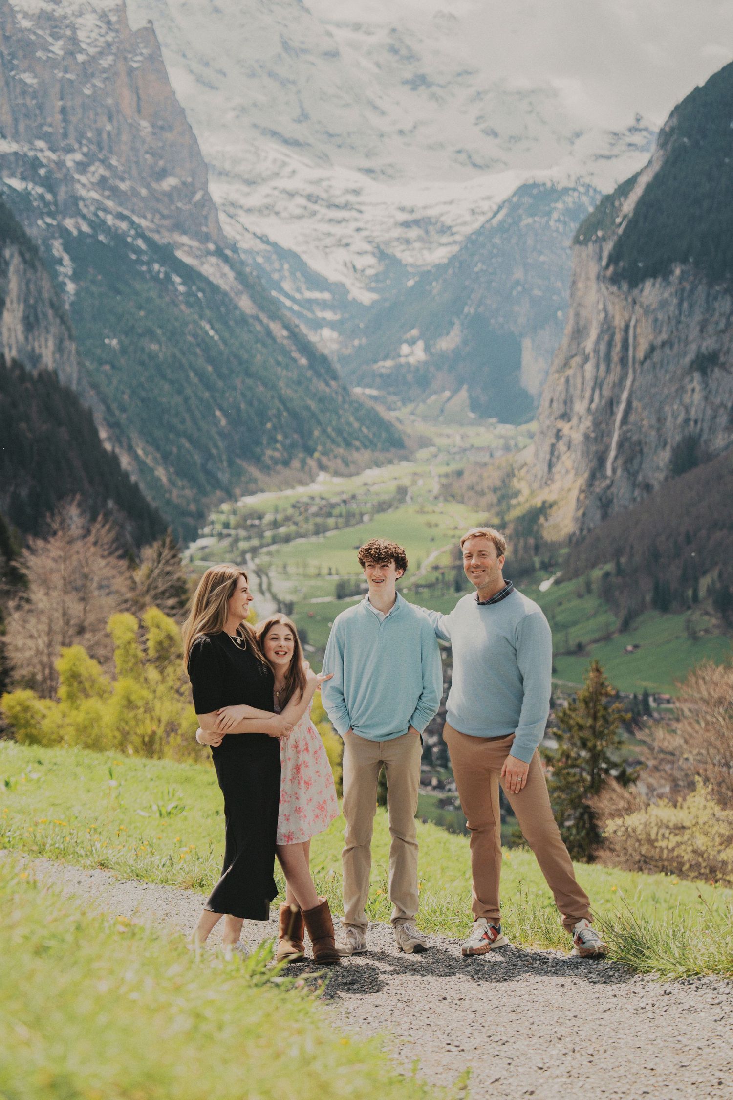Family of four posing on a mountain path with stunning Lauterbrunnen valley and snow-capped Swiss Alps in the background.