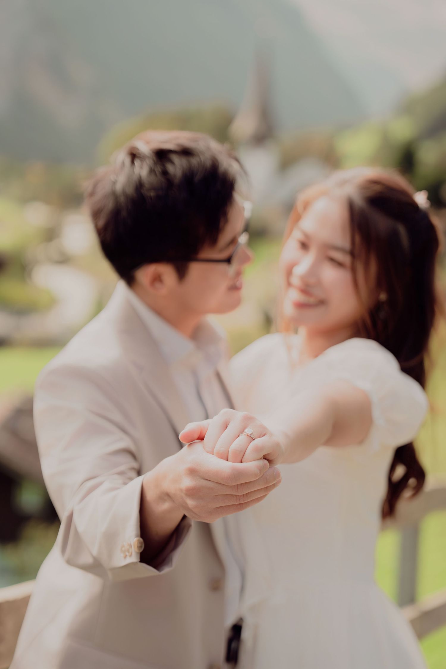 Couple holding hands and smiling at each other with blurred Swiss alpine village in background.