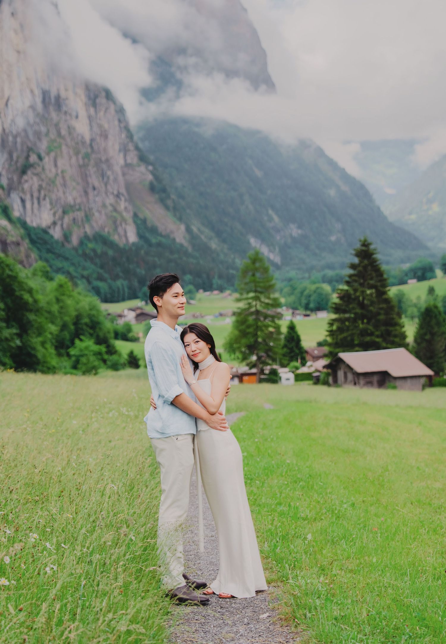 Couple embraces on a grassy path in Lauterbrunnen valley, surrounded by dramatic Swiss Alps and green meadows.