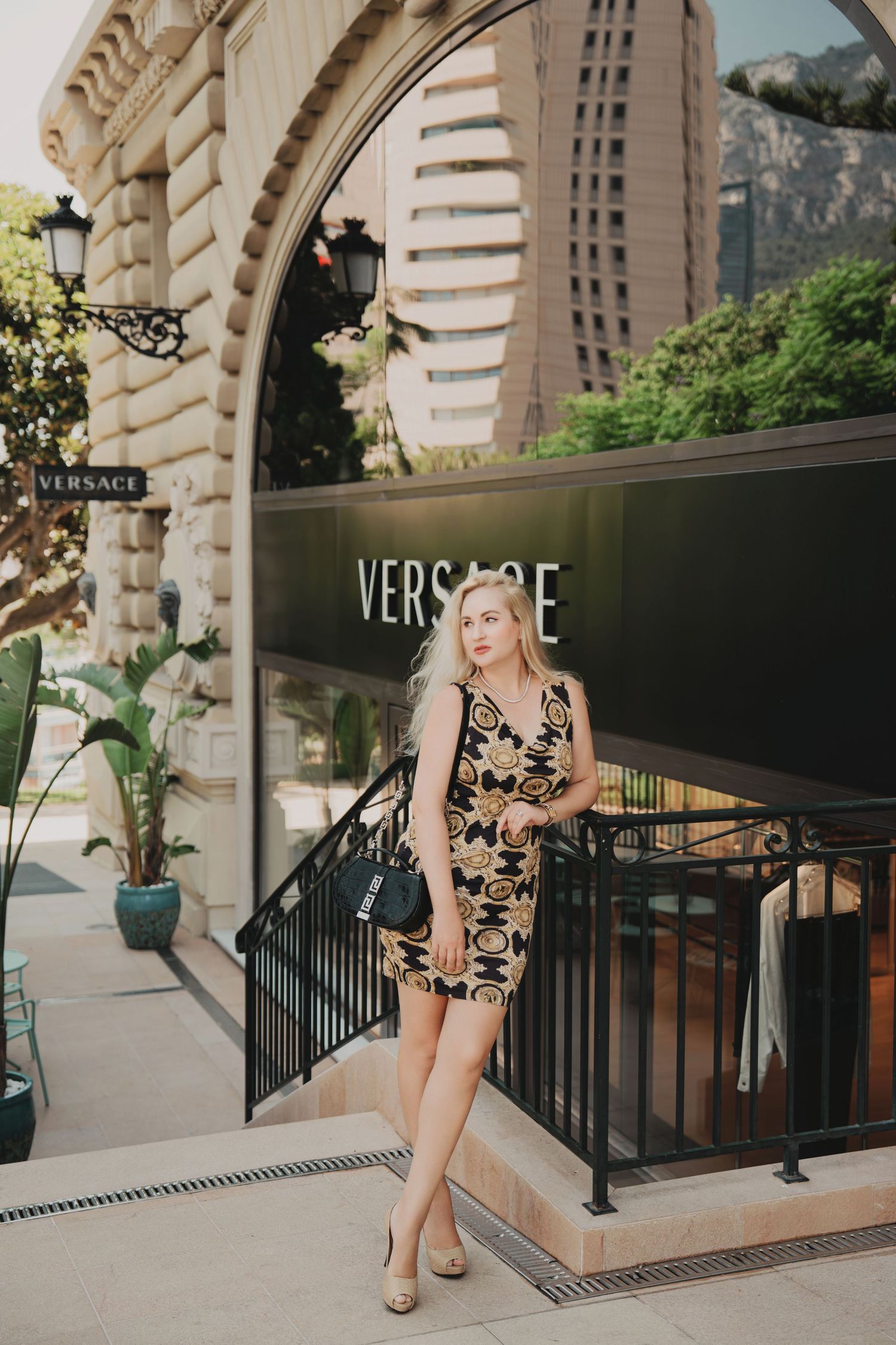 Blonde woman in Versace print dress posing outside Versace store in Monaco.