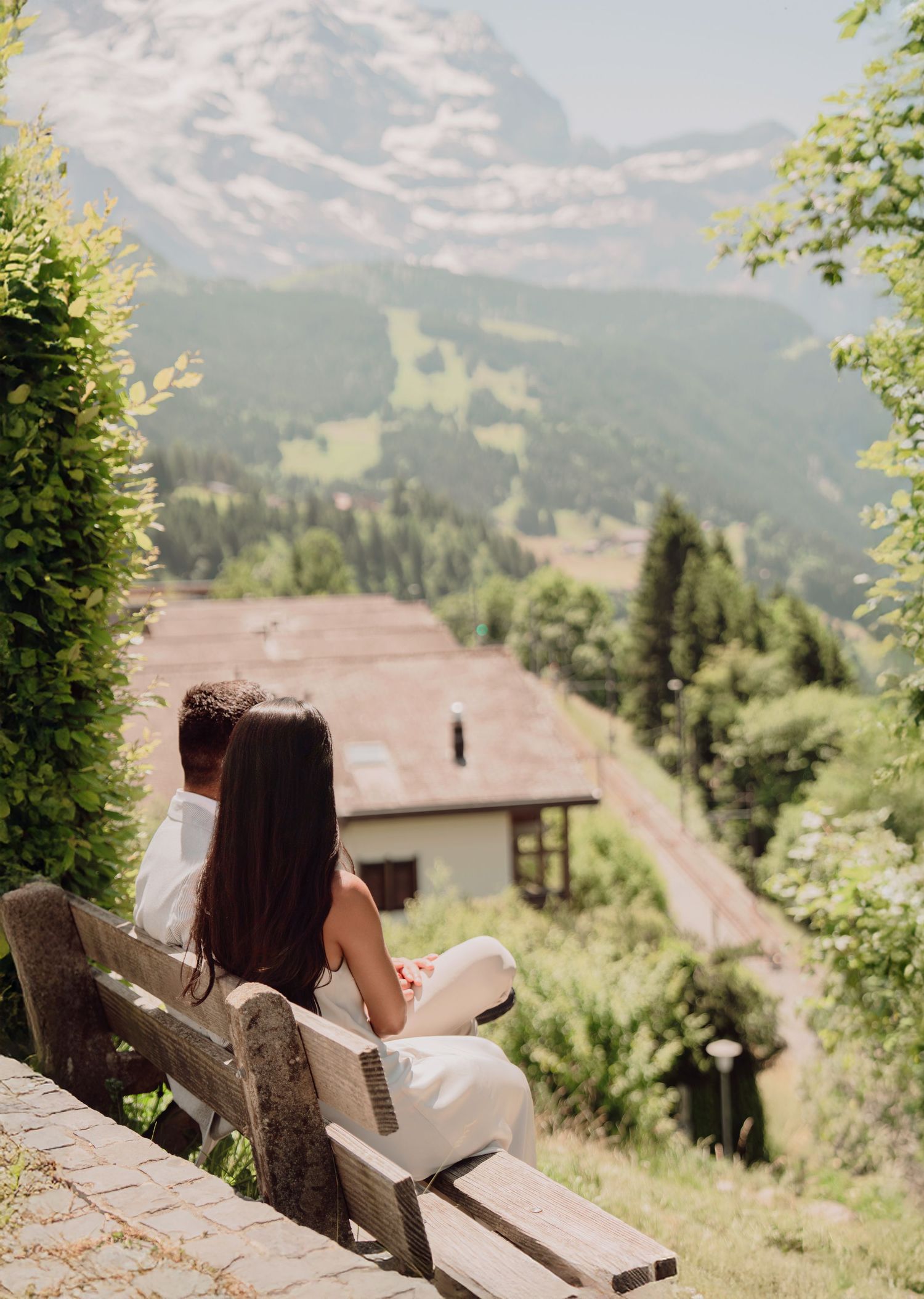 Couple sitting on a wooden bench enjoying a scenic Alpine mountain valley view in Switzerland.