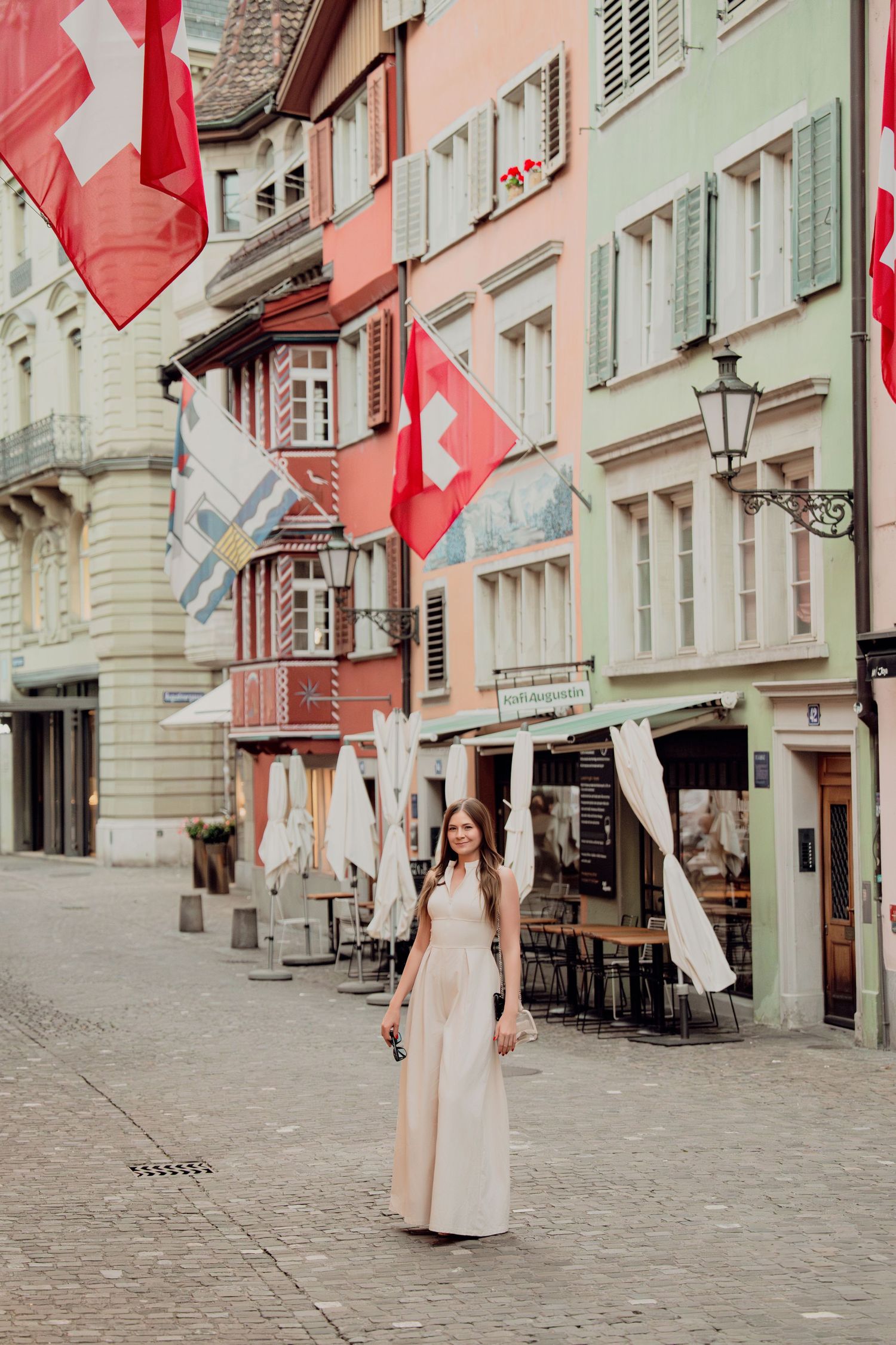 Elegant woman in beige dress strolls flag-lined pedestrian street with colorful buildings in Zurich oldtown.
