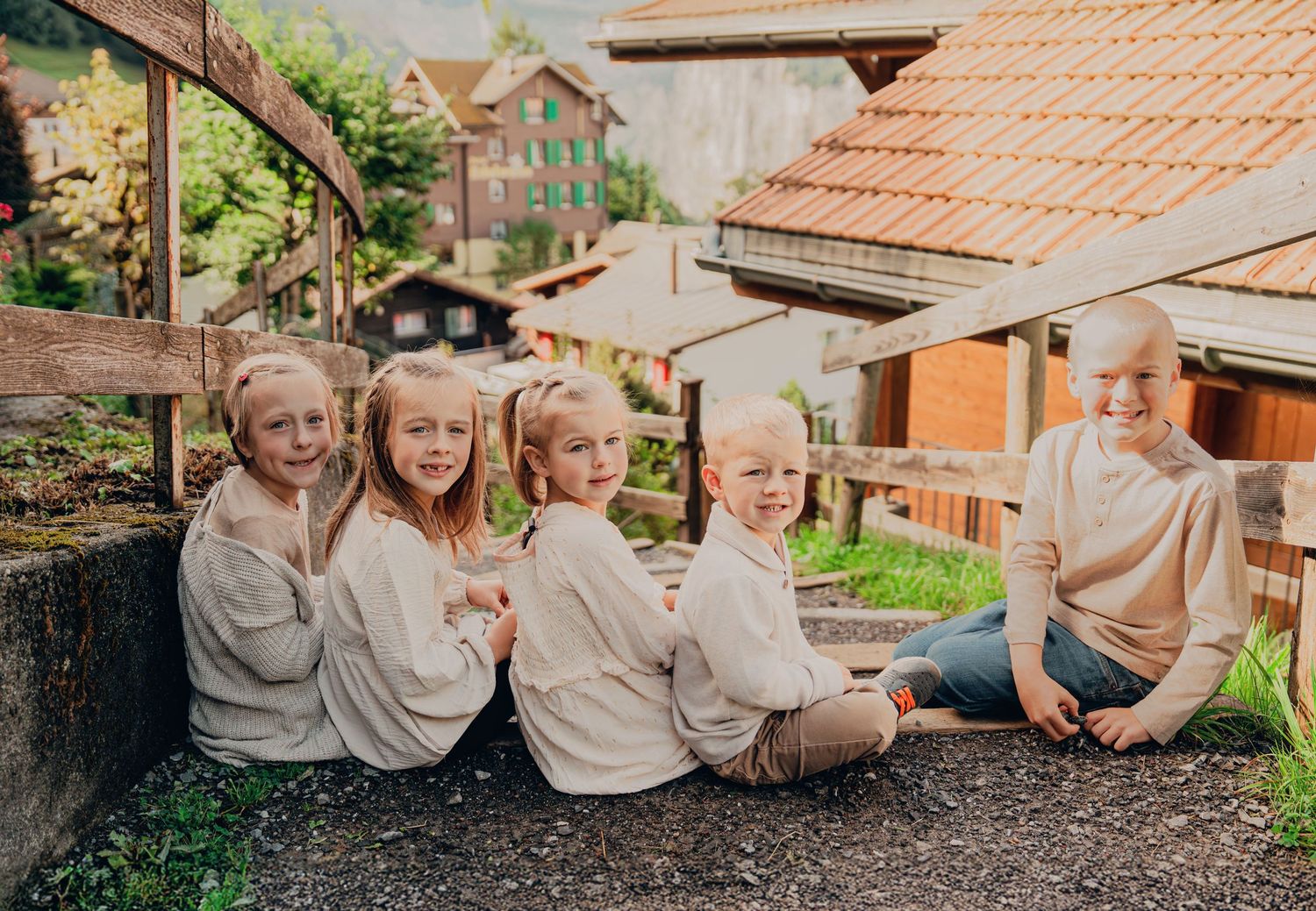 Five blonde children and a bald man sitting together on a stone wall in a Swiss village.