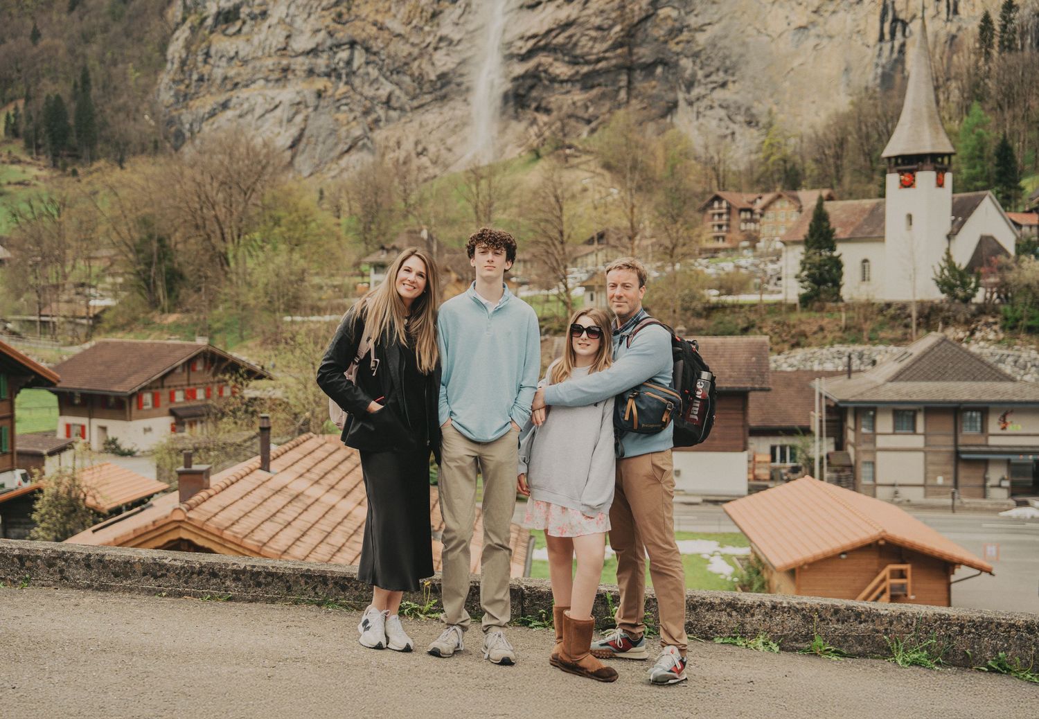Family posing together in front of Lauterbrunnen village with a waterfall and church in background.