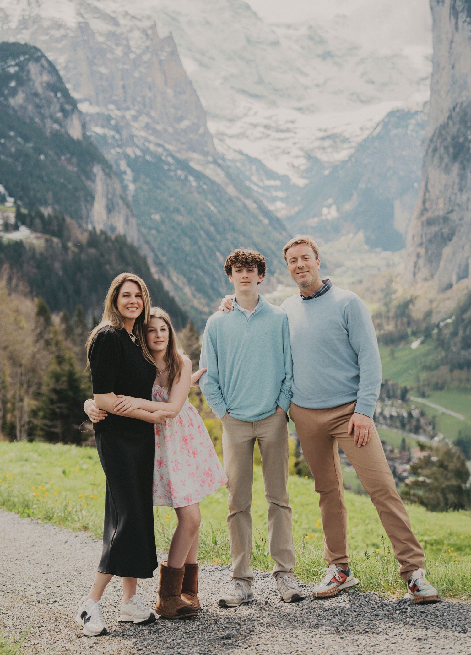Family of four poses together on scenic mountain path overlooking lush Swiss Alps valley in spring.