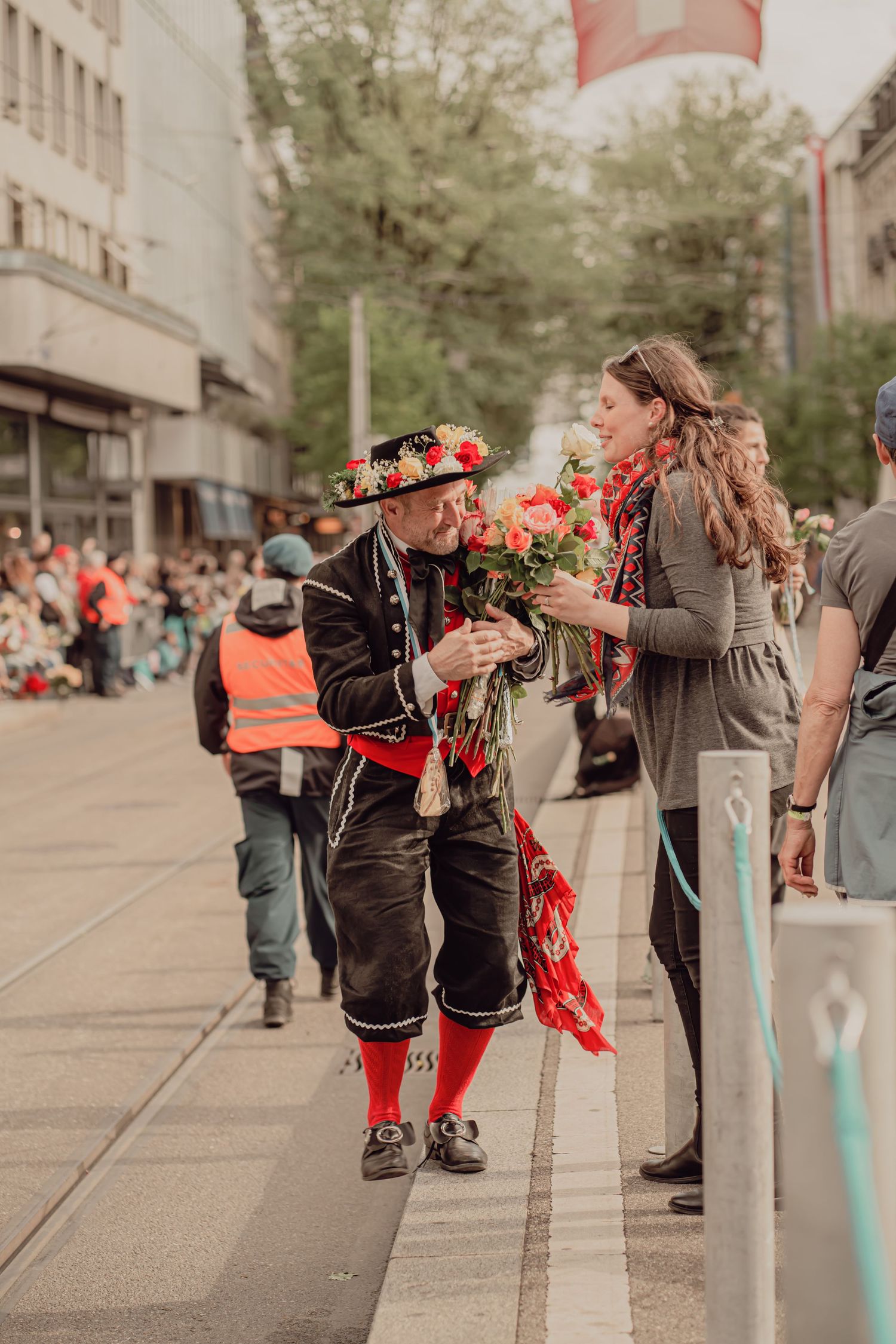 Man in traditional Swiss costume offers roses to a woman at a colorful street parade festival.