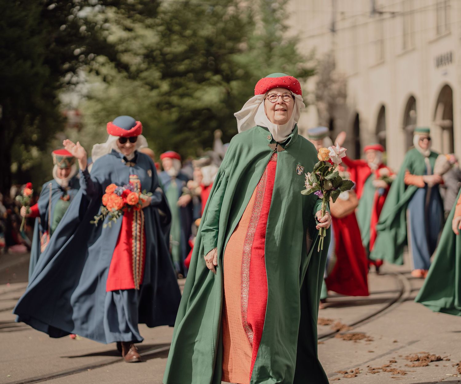 Participants in colorful green and red medieval robes marching joyfully in a traditional street parade.