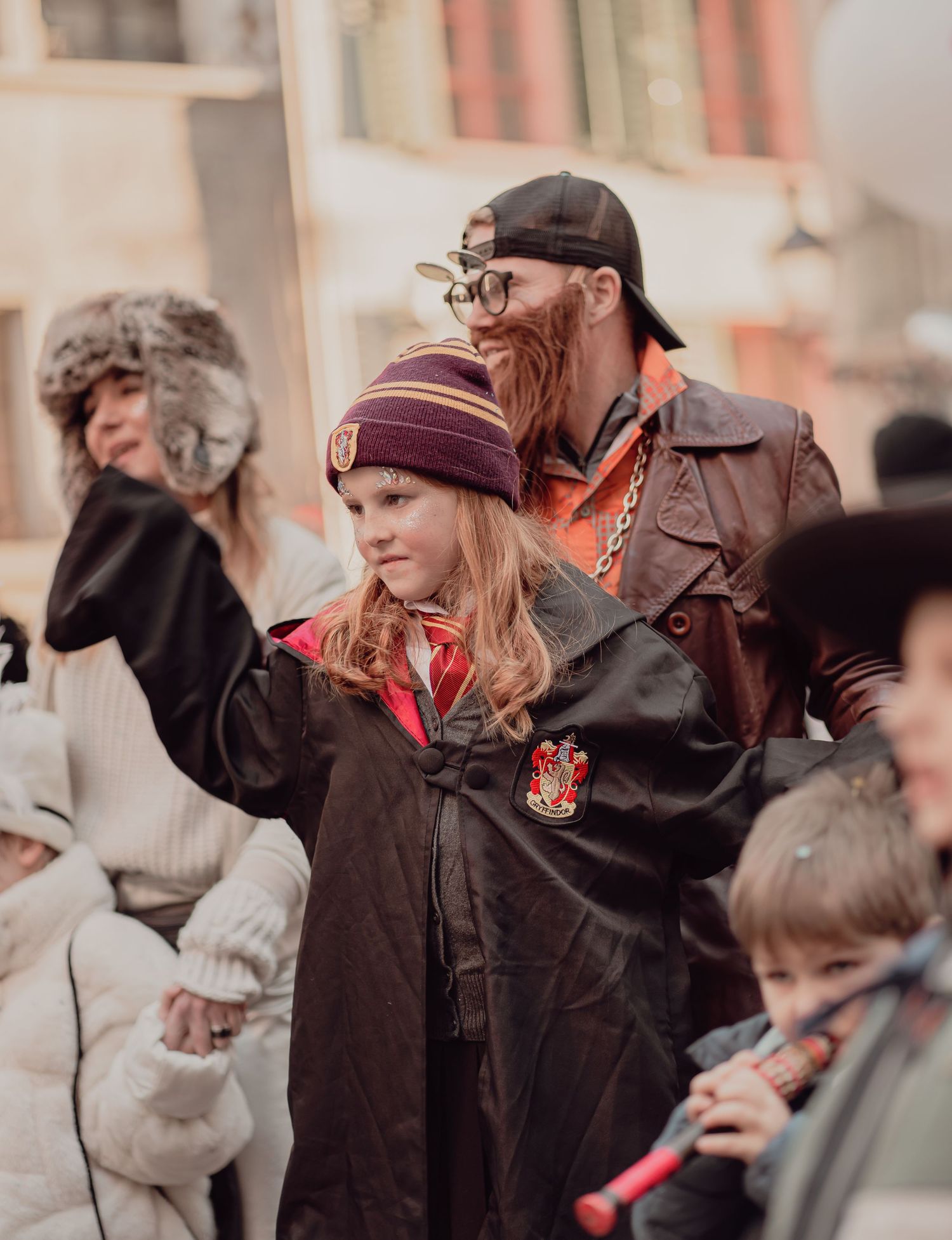 Child in Hogwarts costume with adult in steampunk outfit at carnival parade.