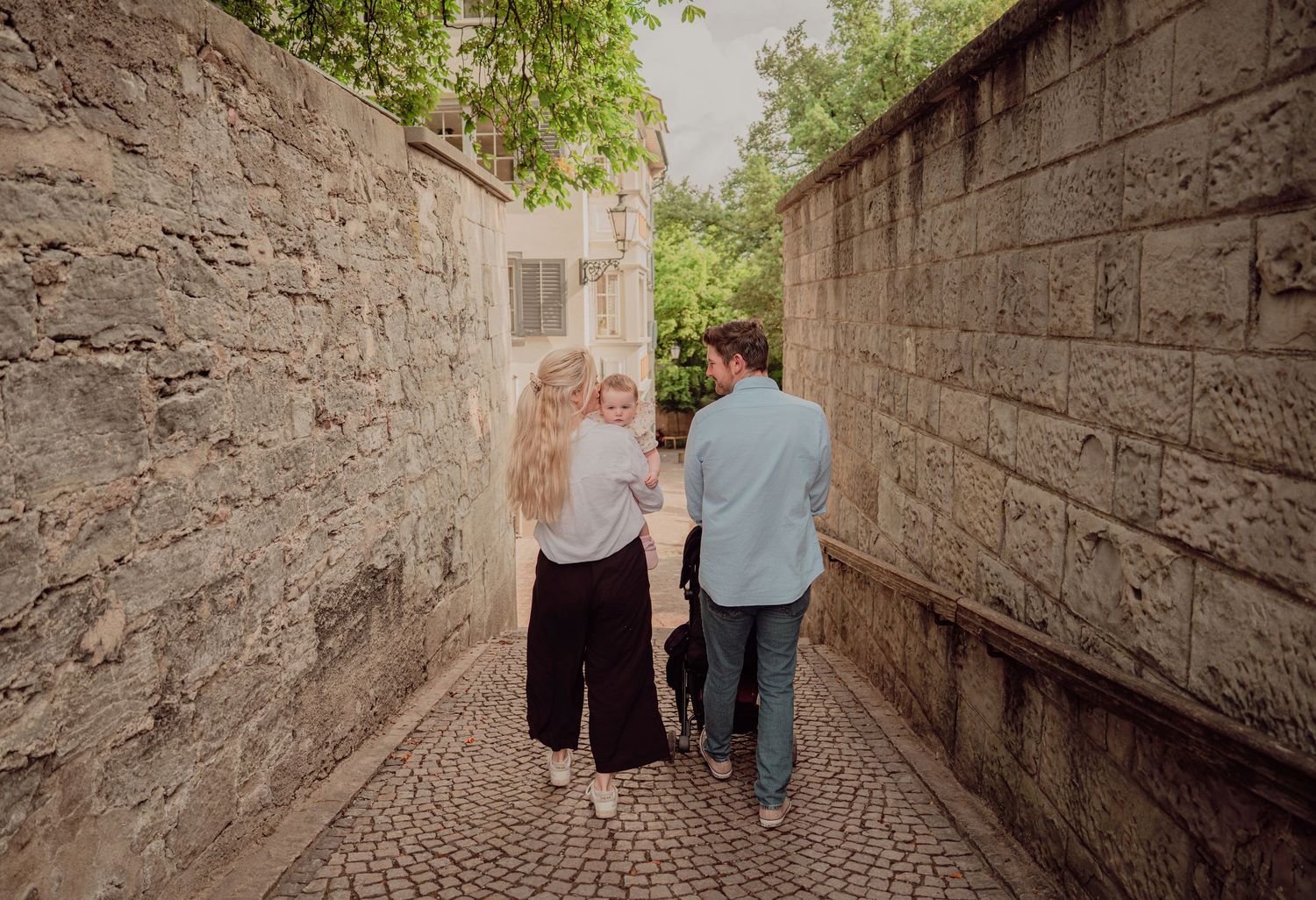 Couple walking hand in hand with baby through a narrow cobblestone alley between stone walls.