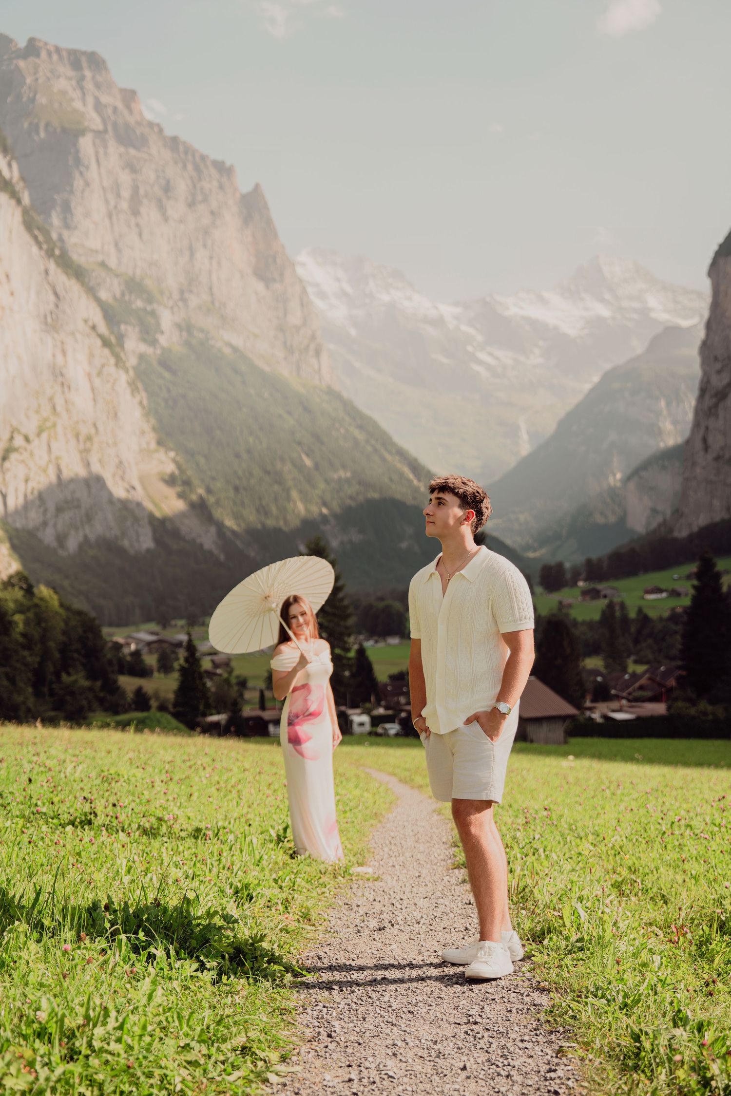 Man in white shirt standing on alpine path with woman holding parasol in Lauterbrunnen, Switzerland.