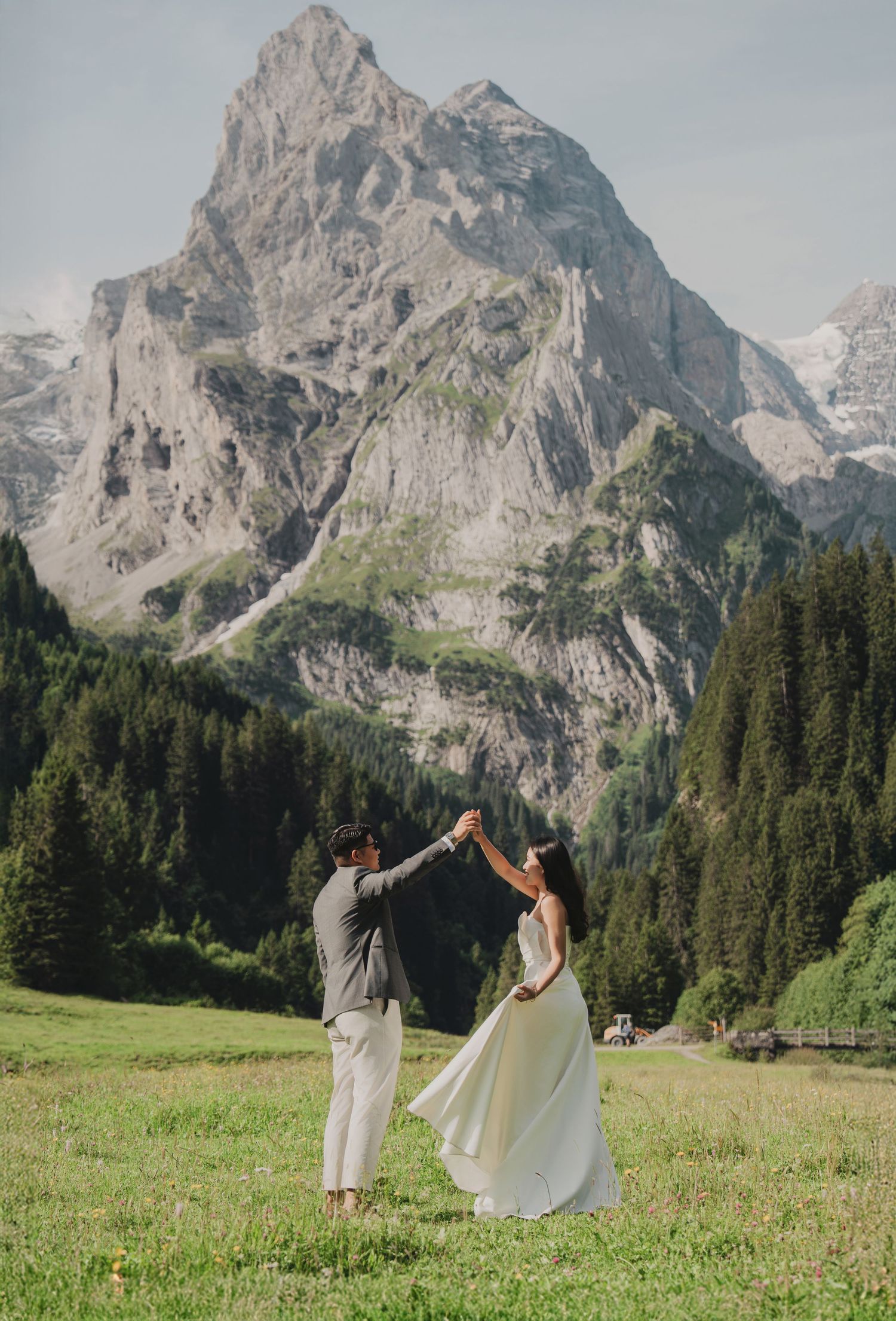 Couple dancing joyfully in mountain meadow with dramatic rocky peak towering in the background.
