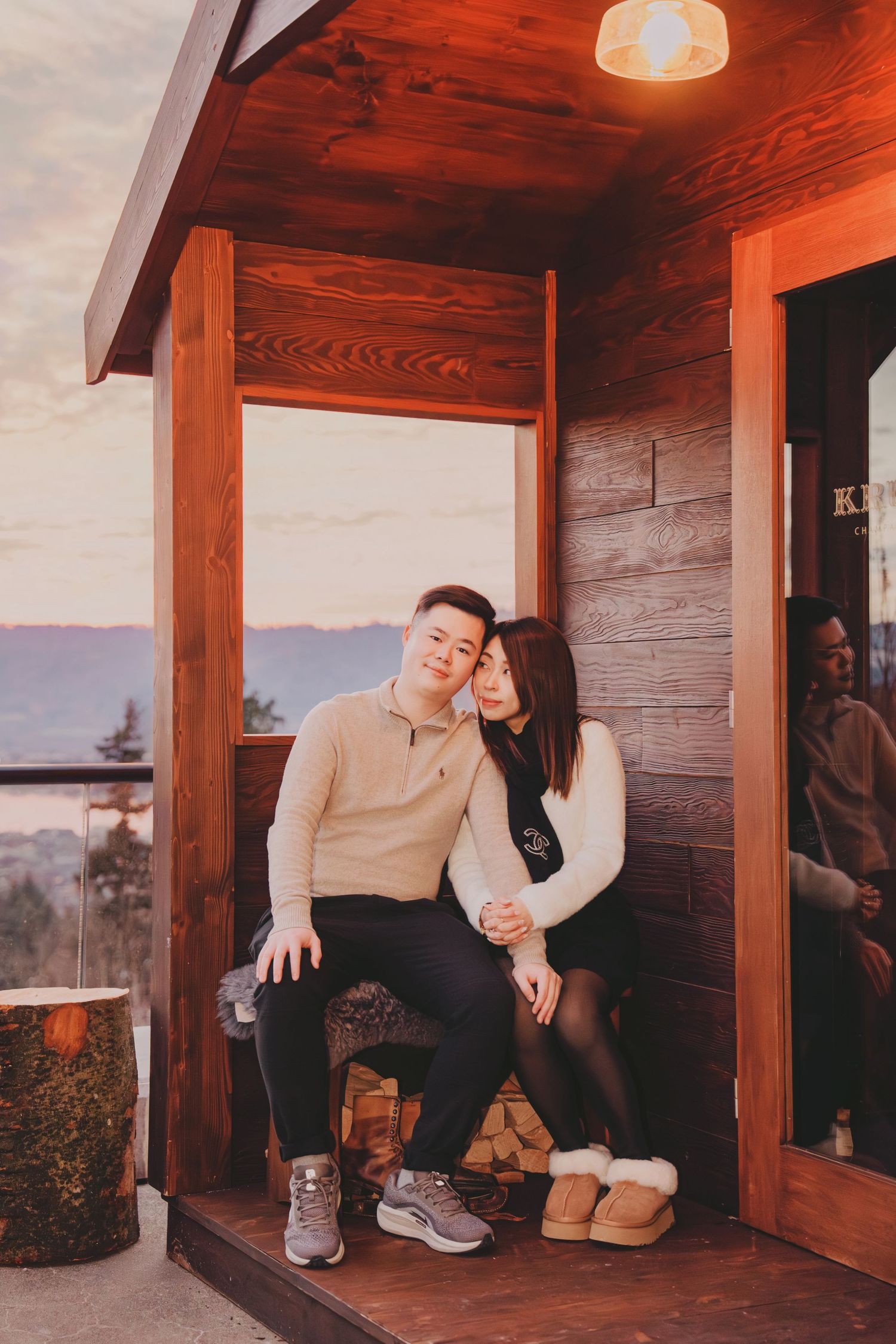 Couple cuddling on wooden cabin porch steps at dusk with mountain valley views behind them.