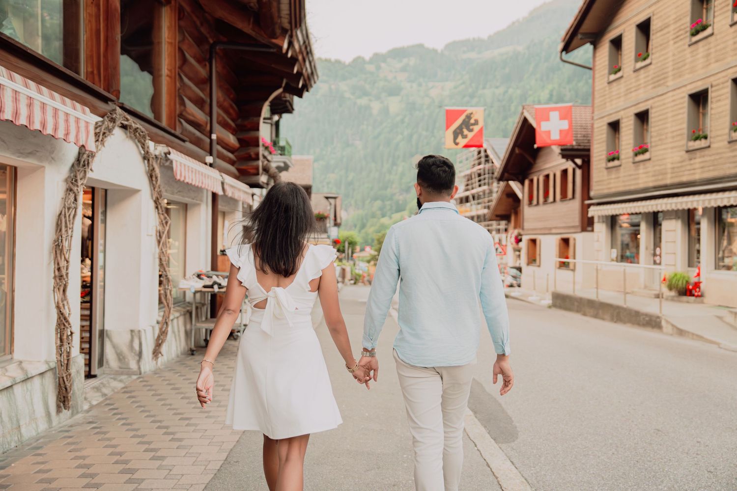 Couple walking hand in hand down a charming Swiss alpine village street with mountain views and Swiss flags.