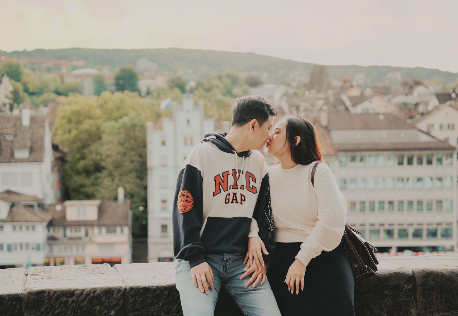 Asian couple sharing a romantic moment on a terrace with Zurich cityscape in the background.
