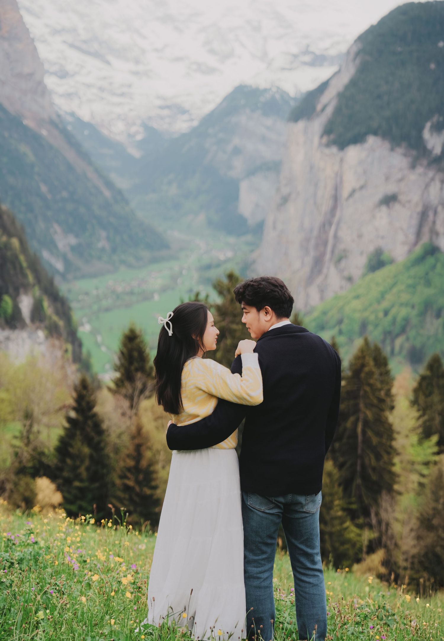 Romantic couple embracing in Swiss alpine meadow with Lauterbrunnen valley and snow-capped peaks behind.