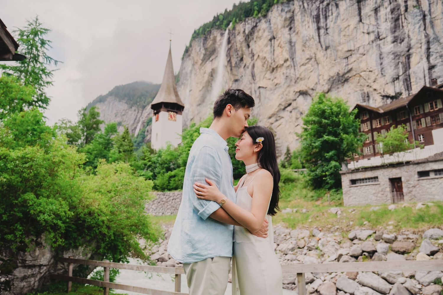 Couple embracing romantically in Lauterbrunnen Switzerland with waterfall and alpine village in background.
