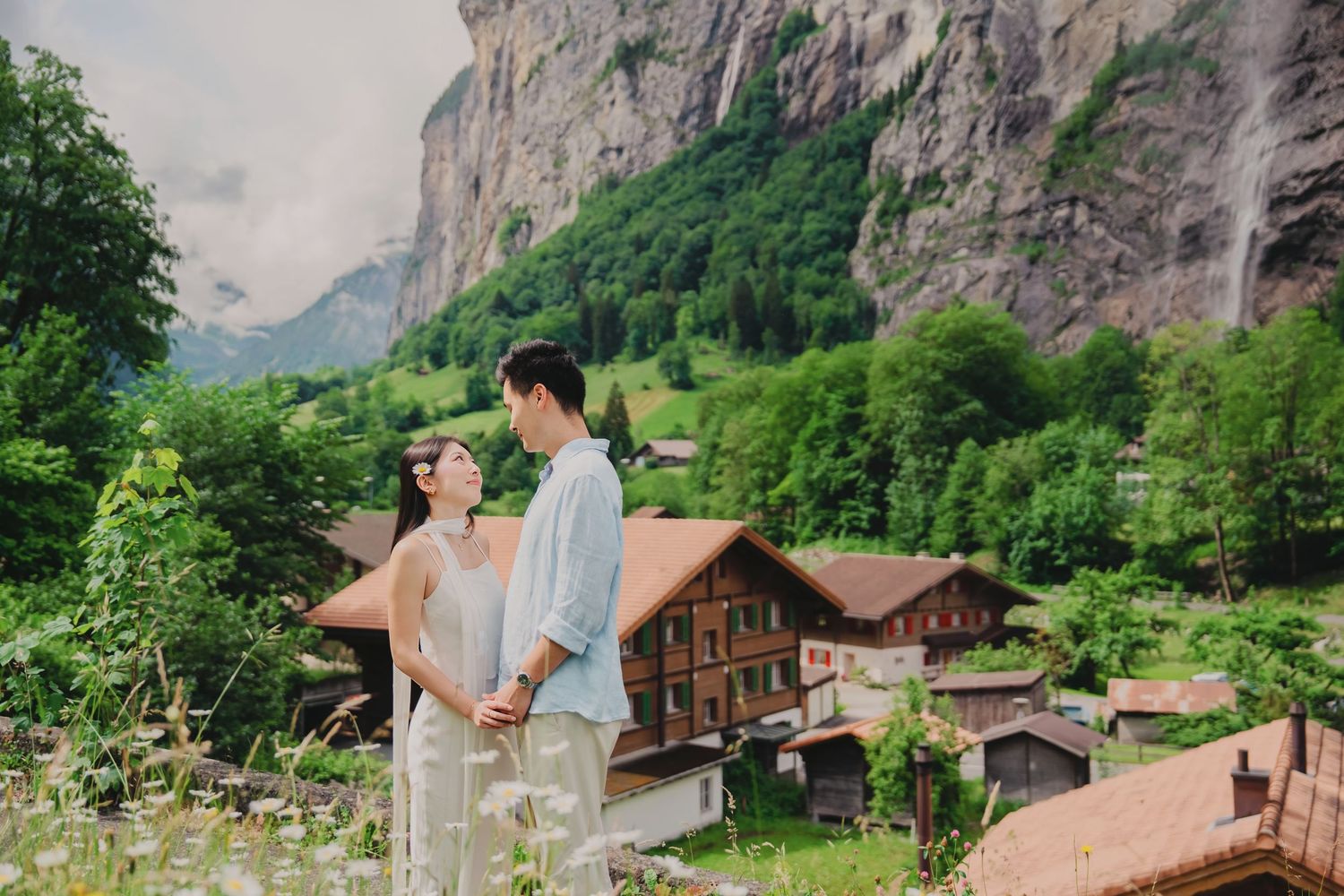 Couple holds hands while admiring the Staubbach waterfall and Swiss village of Lauterbrunnen in the background.