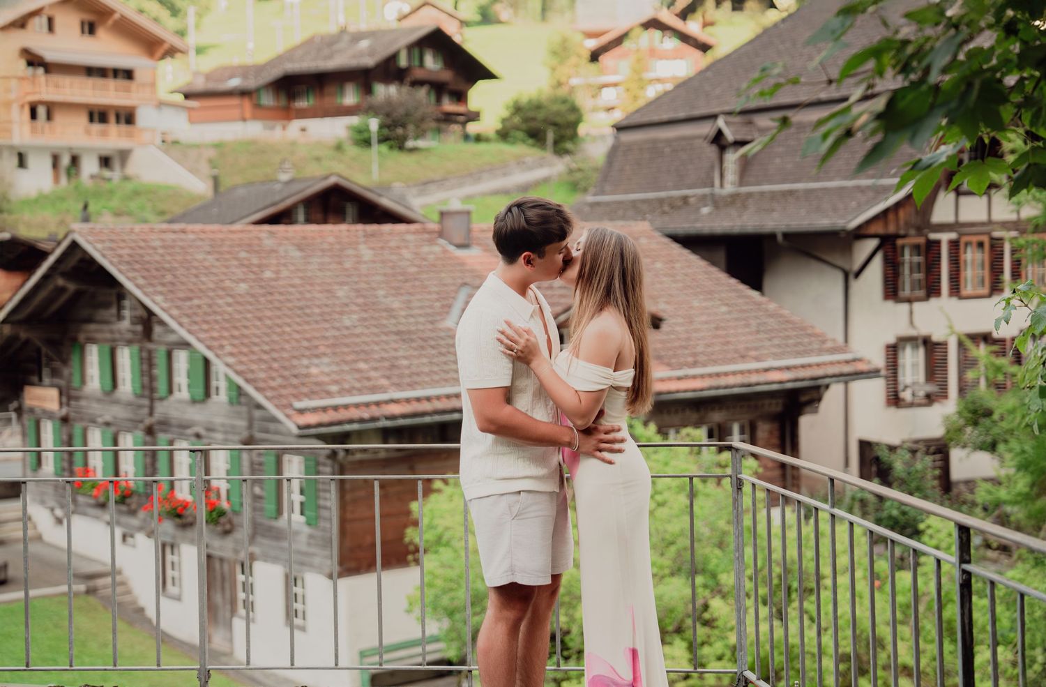 Couple kissing tenderly on a balcony with charming Swiss alpine village houses in background.