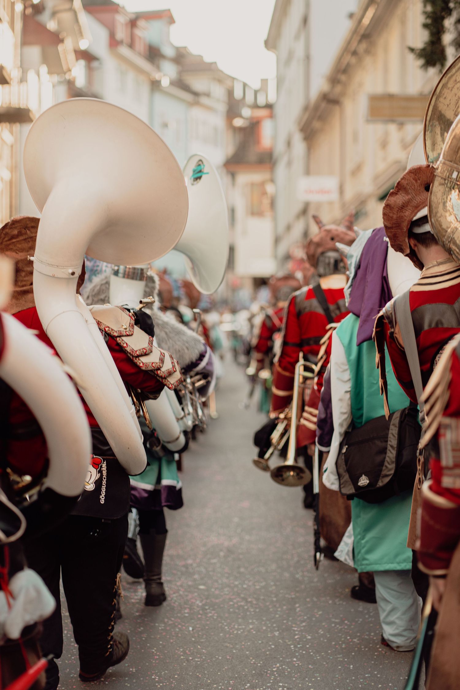 Marching band in colorful costumes with brass instruments walks through a narrow street.