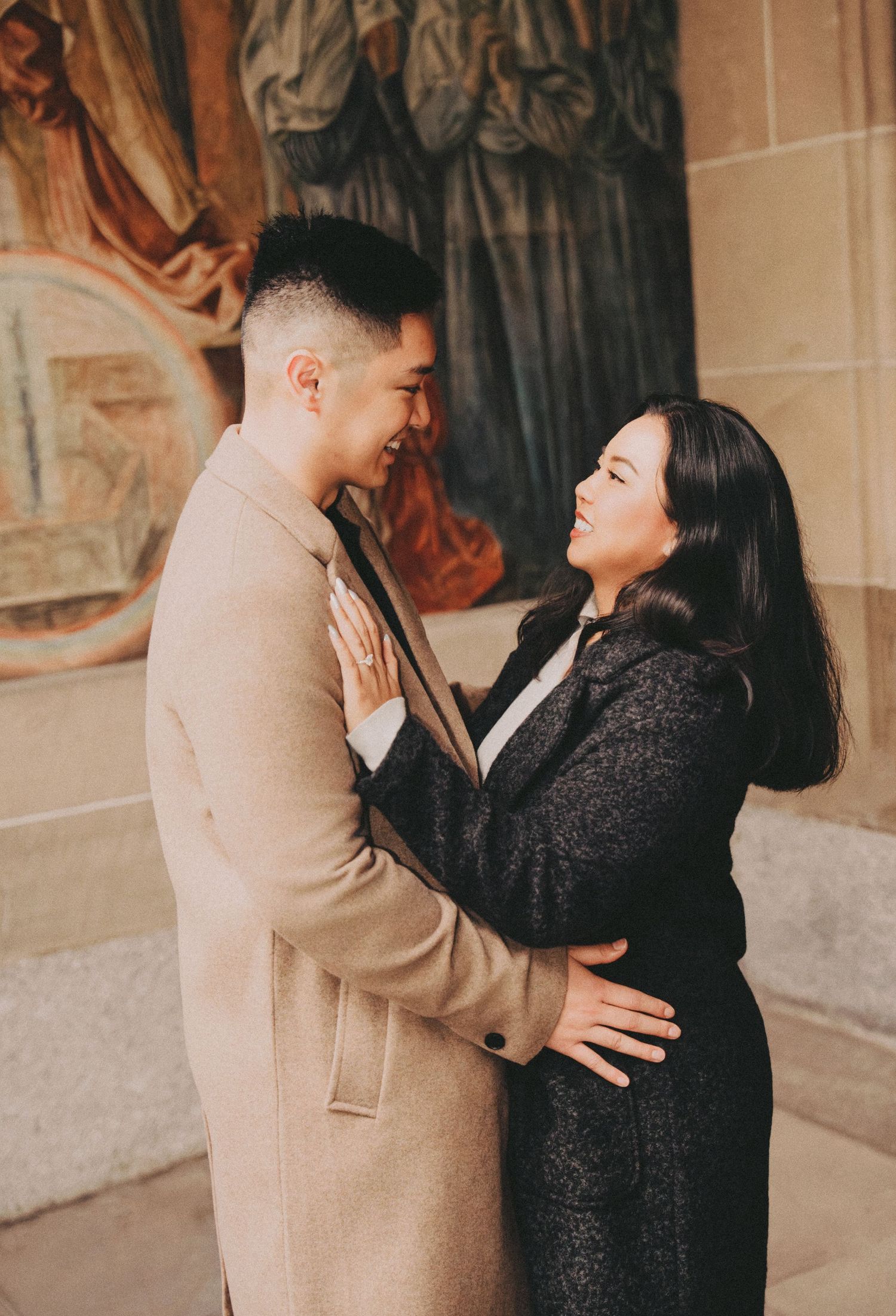 Couple sharing a romantic moment, smiling at each other in front of ornate wall murals.