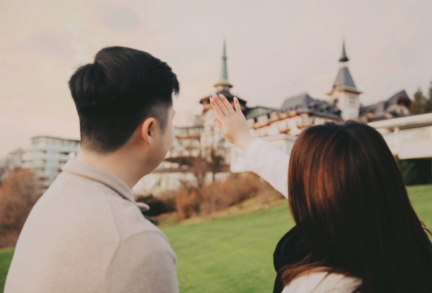 Asian couple viewing engagement ring with turret-style building in background.