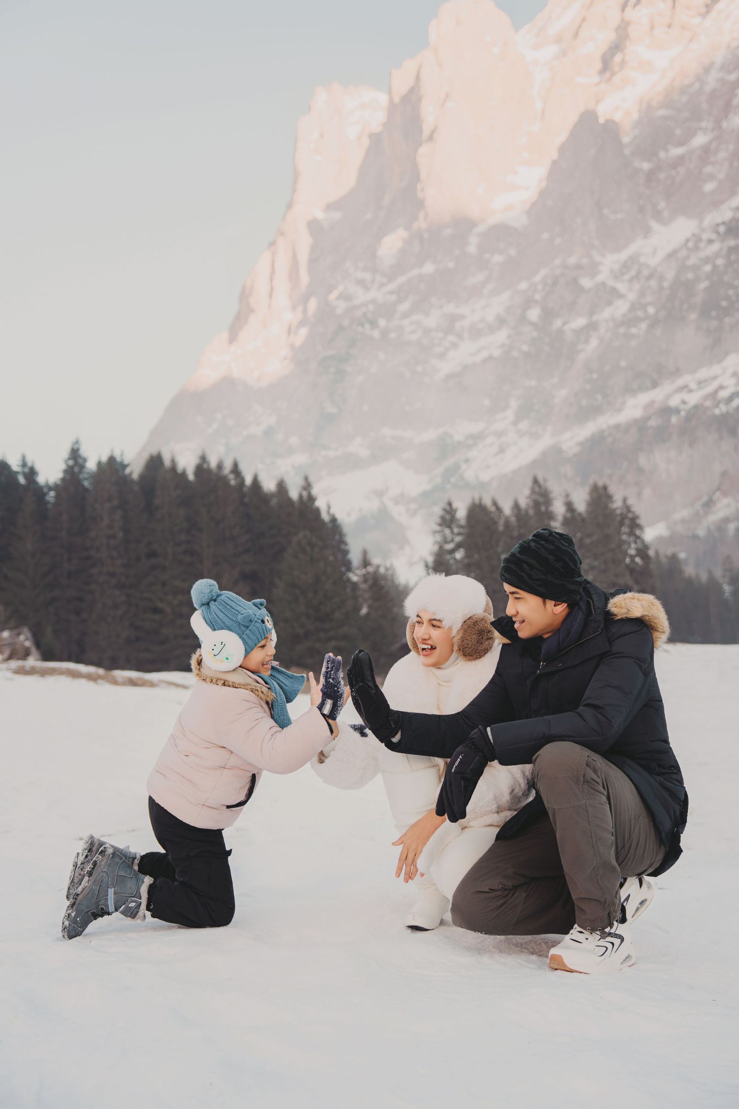 Happy family with young child playing in snow with majestic mountain backdrop on sunny winter day.