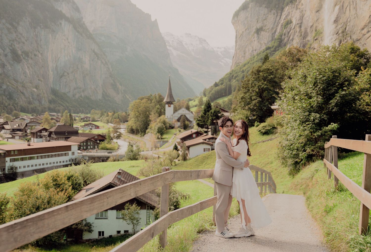 Couple posing together on a hillside path with stunning Lauterbrunnen valley and church in background.