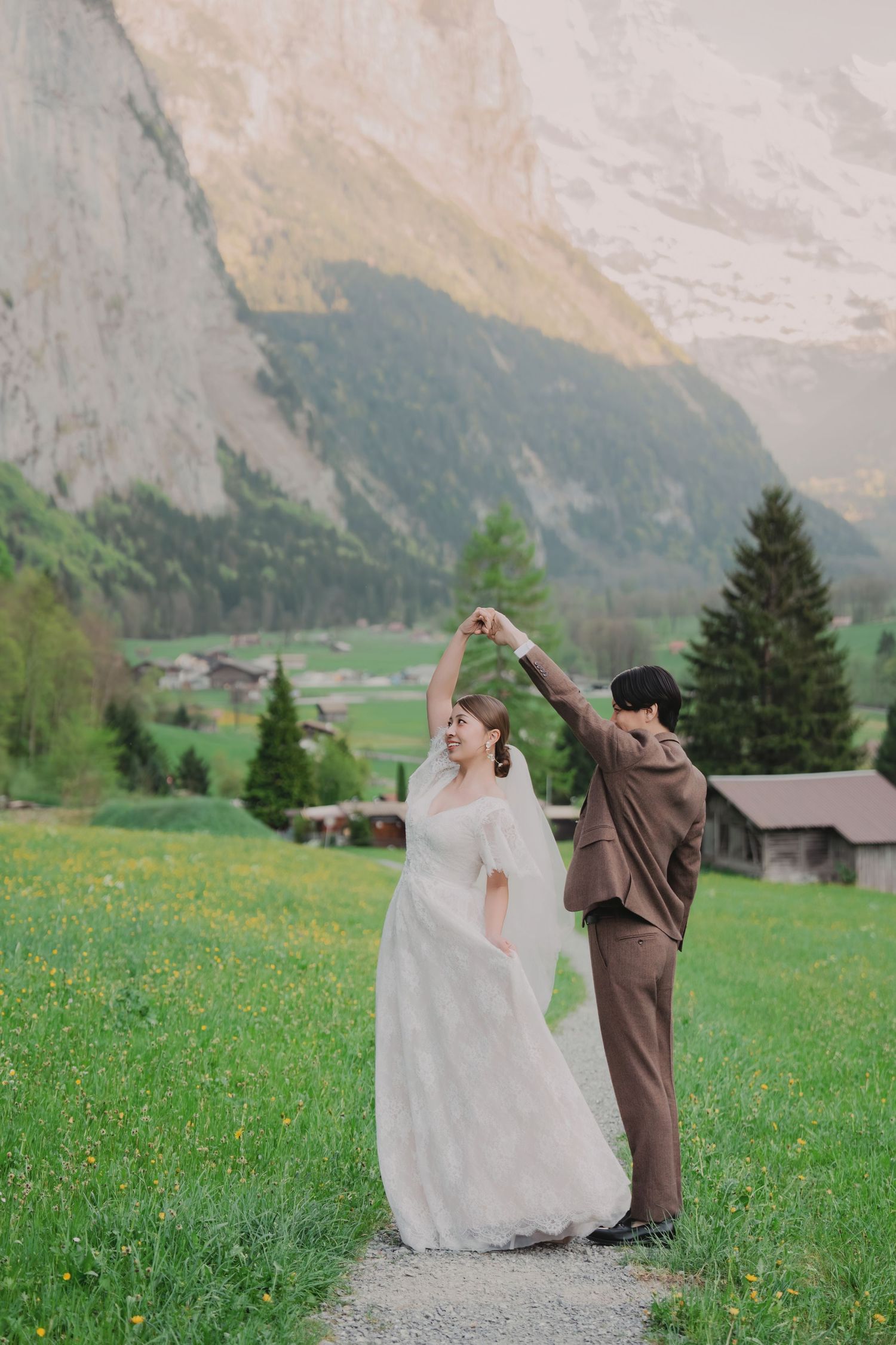 Bride and groom dancing joyfully in a lush green Swiss alpine meadow with majestic mountain scenery behind them.