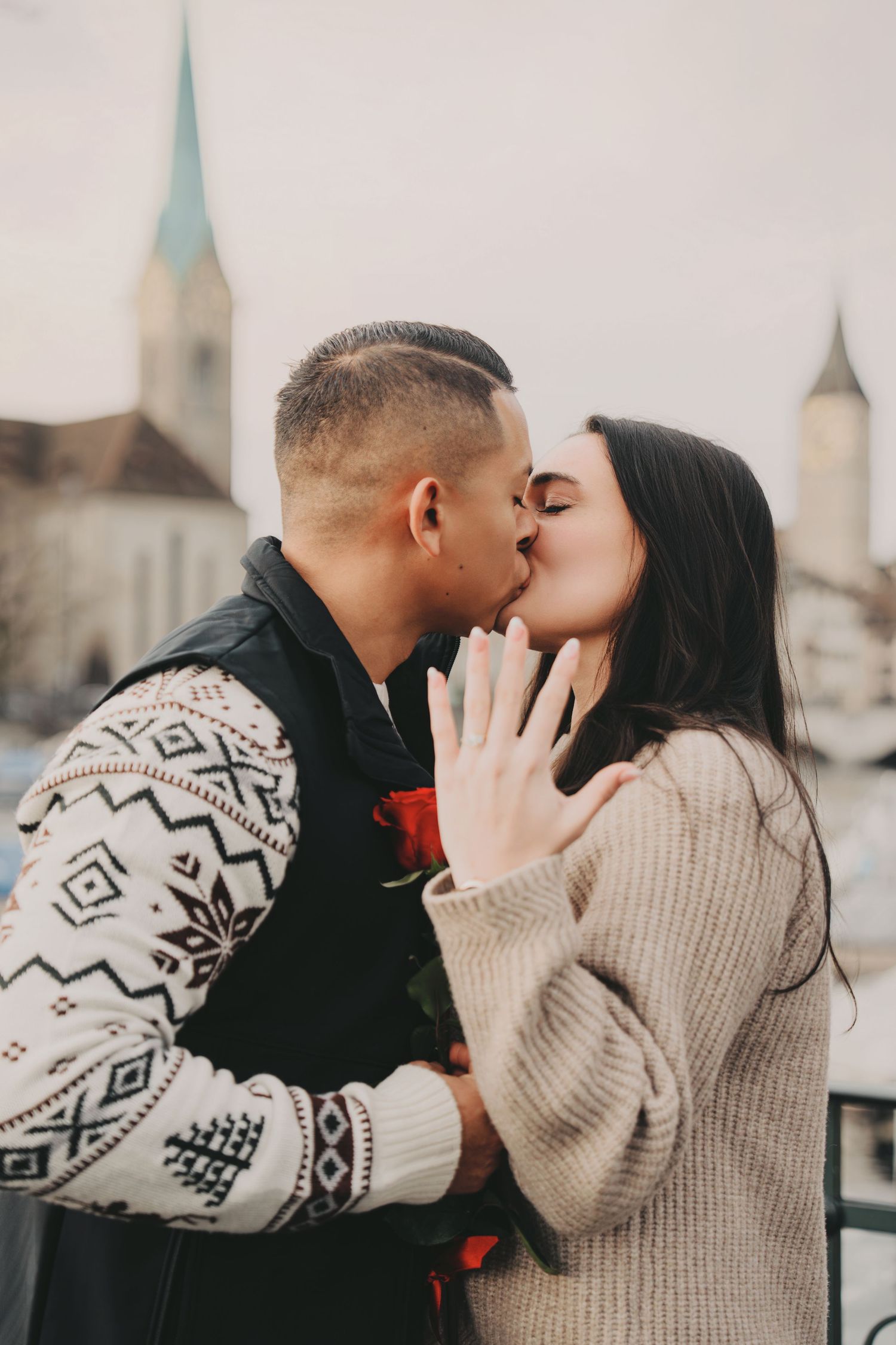Romantic couple sharing a kiss outdoors with Zurich church towers in background.