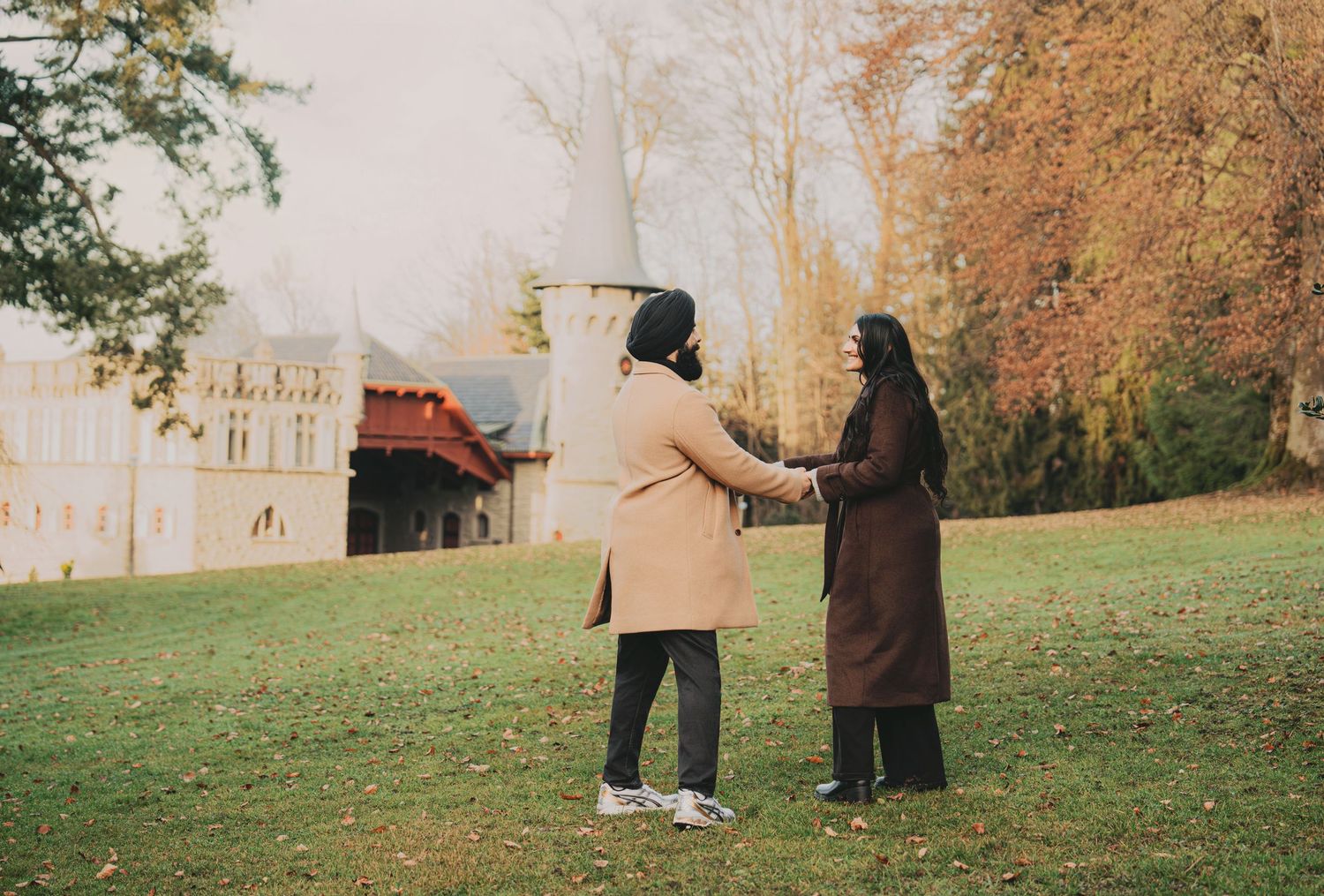 Couple holding hands in autumn park with historic building backdrop.