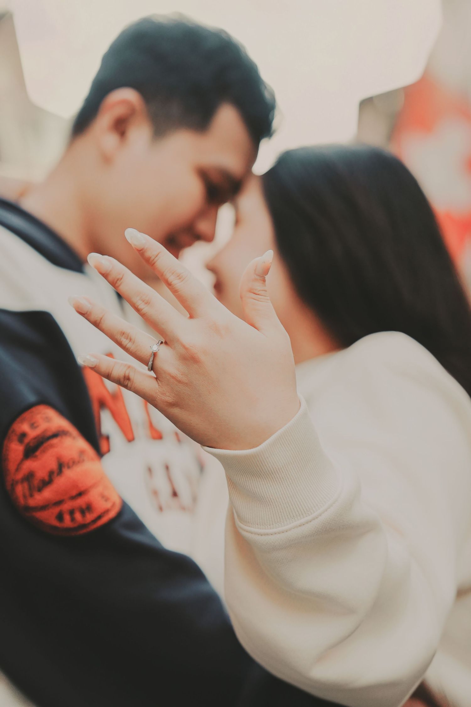 Close-up of engaged couple touching foreheads with woman displaying her engagement ring on her hand.