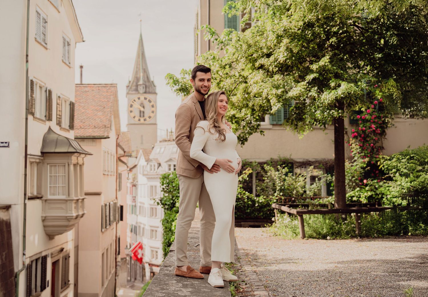 Expecting couple embraces lovingly during maternity photoshoot on sunny cobblestone street in Zurich old town.