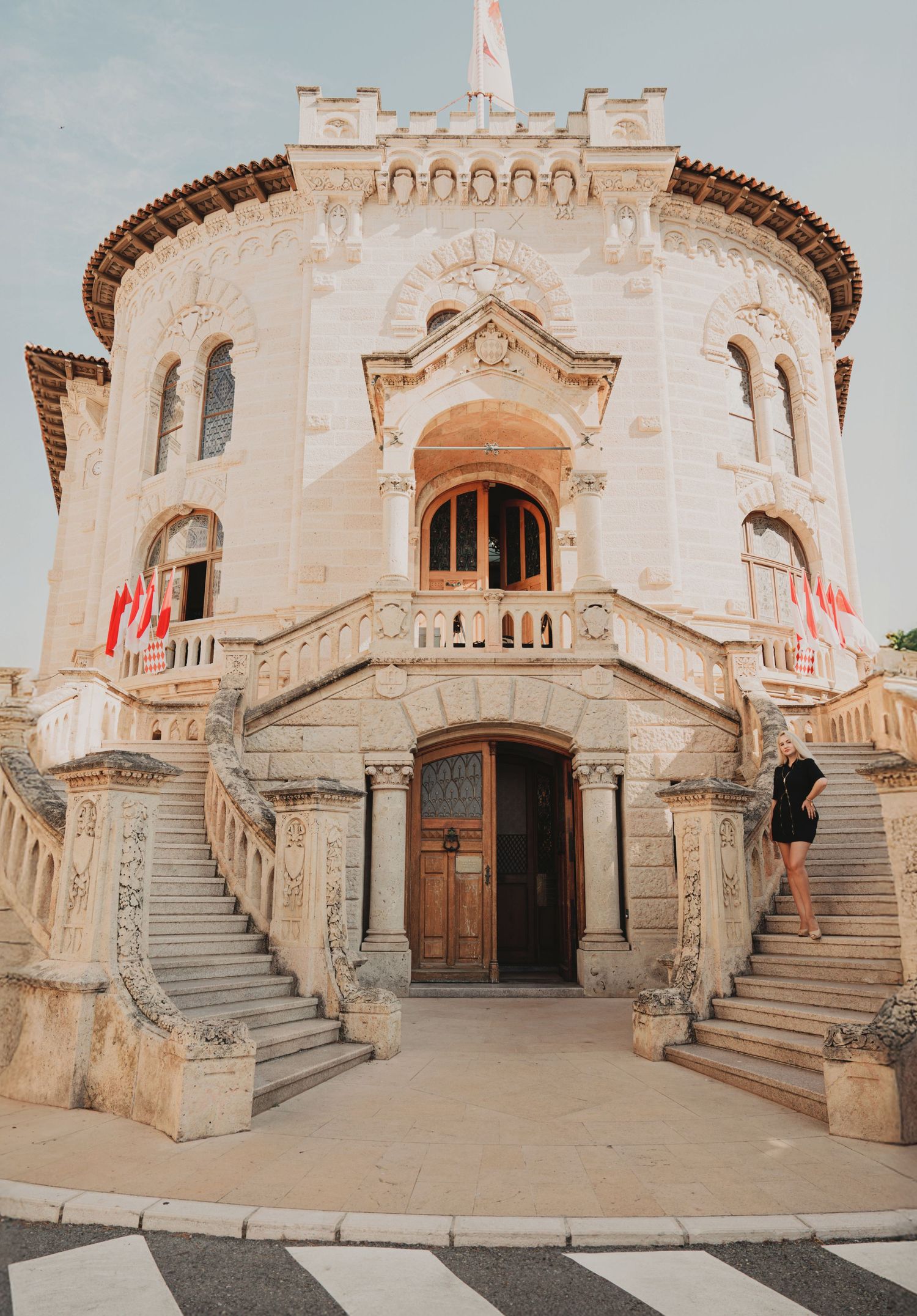 Grand historic Monaco courthouse with twin staircases, ornate facade and red flags.