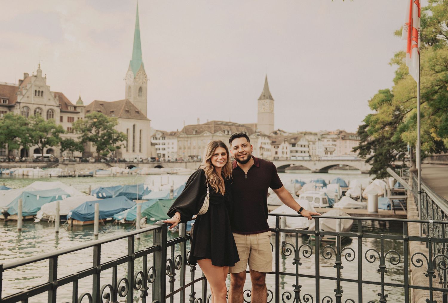 Happy couple embracing on a bridge with Zurich old town skyline, church spires, and harbor behind them.