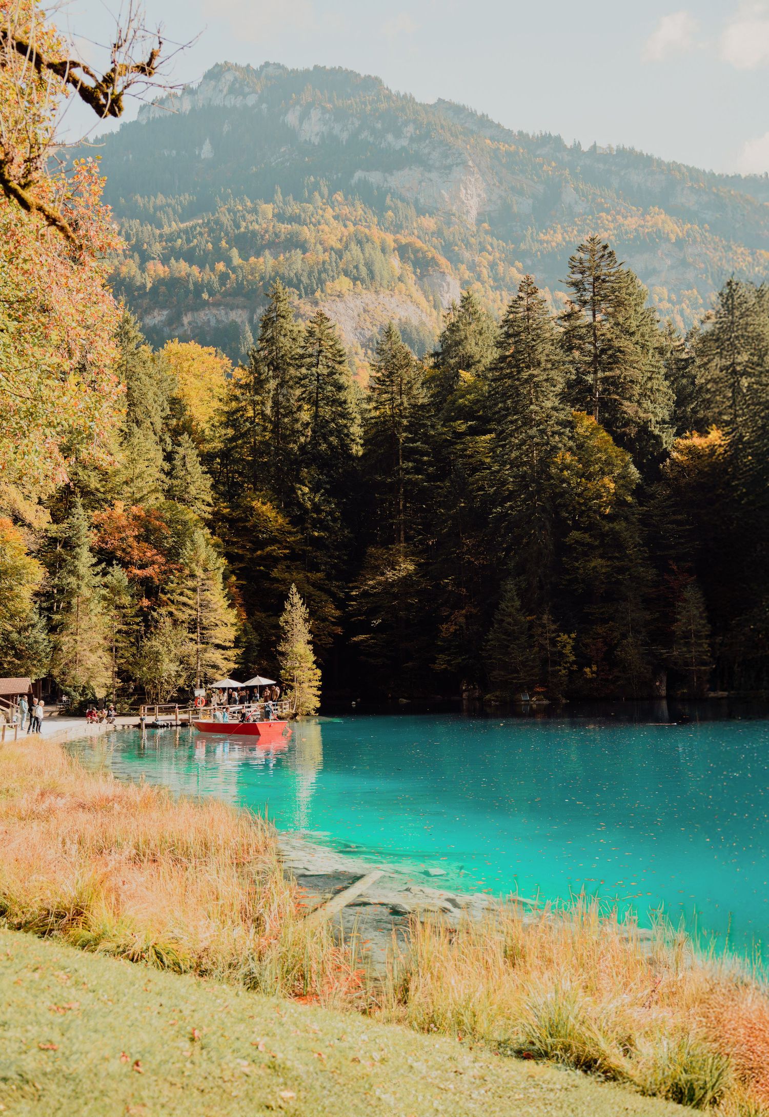 Vibrant turquoise alpine lake with red boats, autumn trees, and misty mountain backdrop in fall.