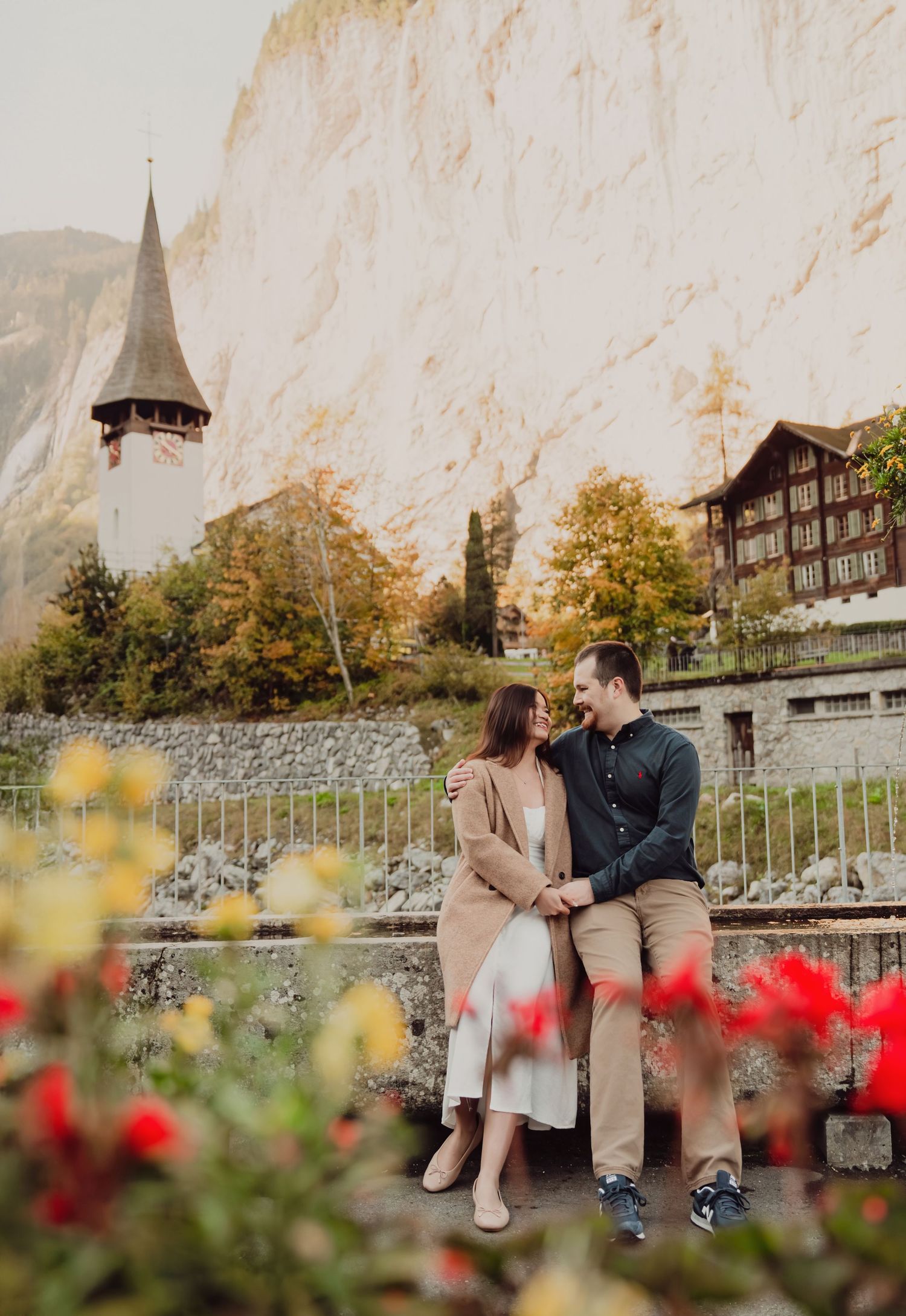 Couple sitting together with colorful flowers, a church steeple, and Swiss cliffs behind.