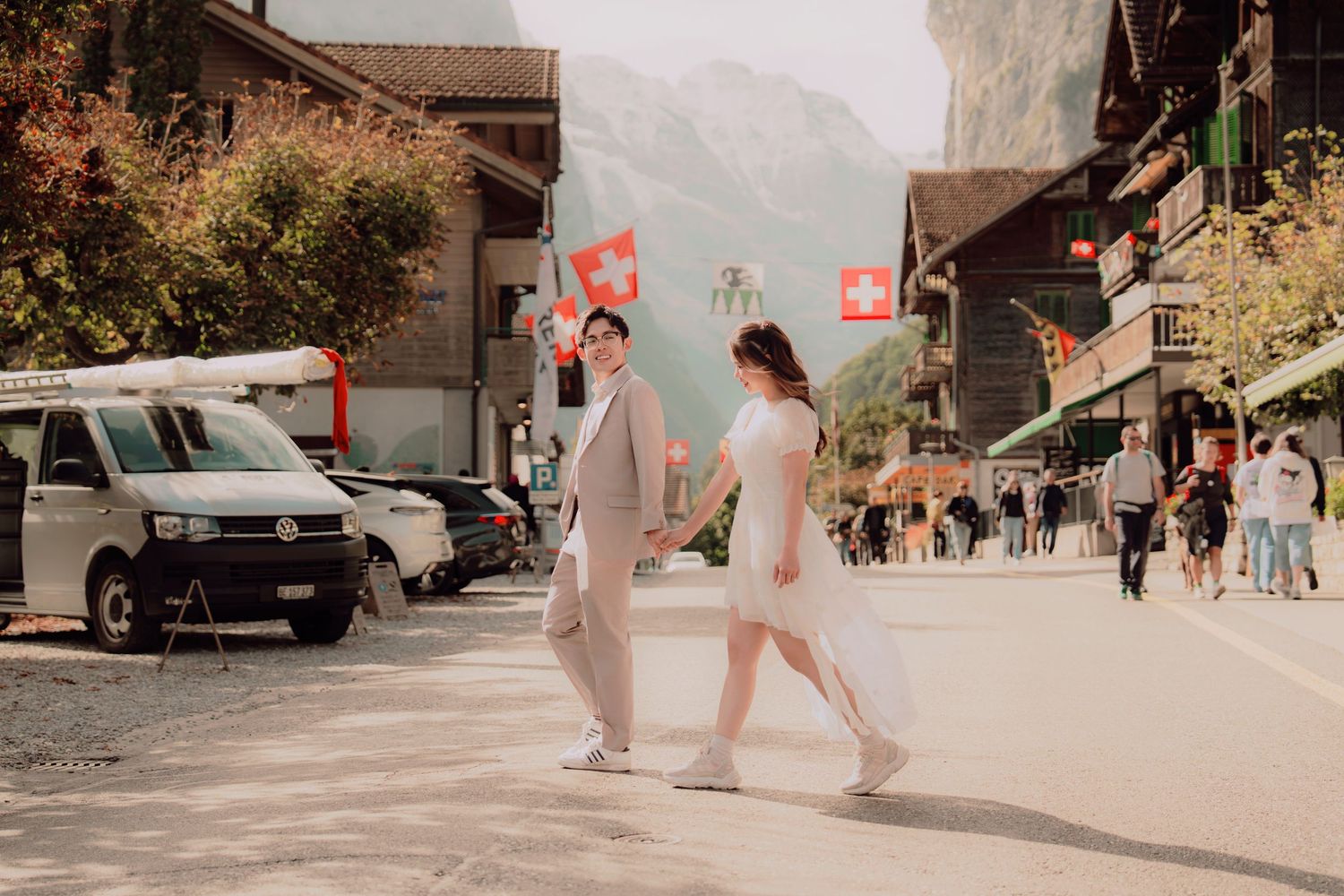 Couple strolling hand in hand along a sunny Lauterbrunnen street lined with Swiss flags and mountains.