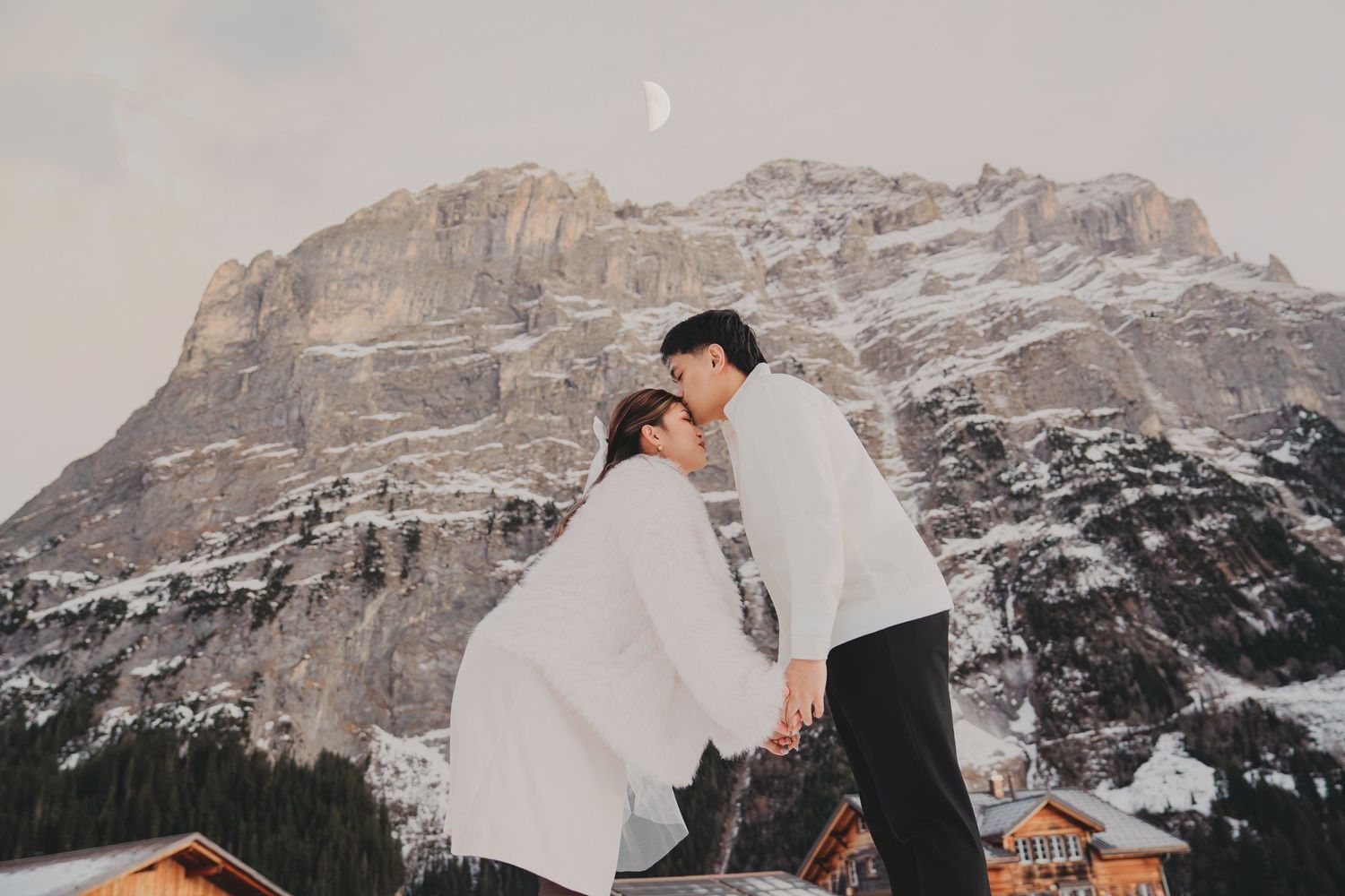 Romantic couple leaning in for a kiss with snowy mountain and crescent moon in background.
