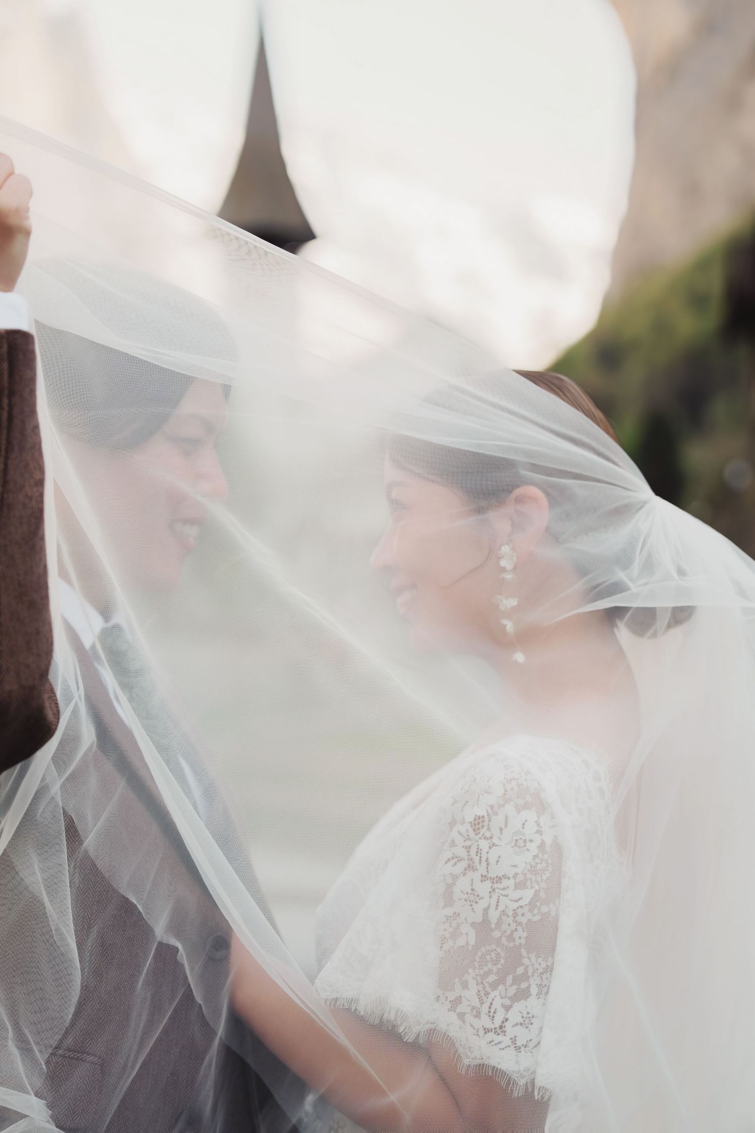 Bride and groom share an intimate moment under a flowing white wedding veil outdoors.