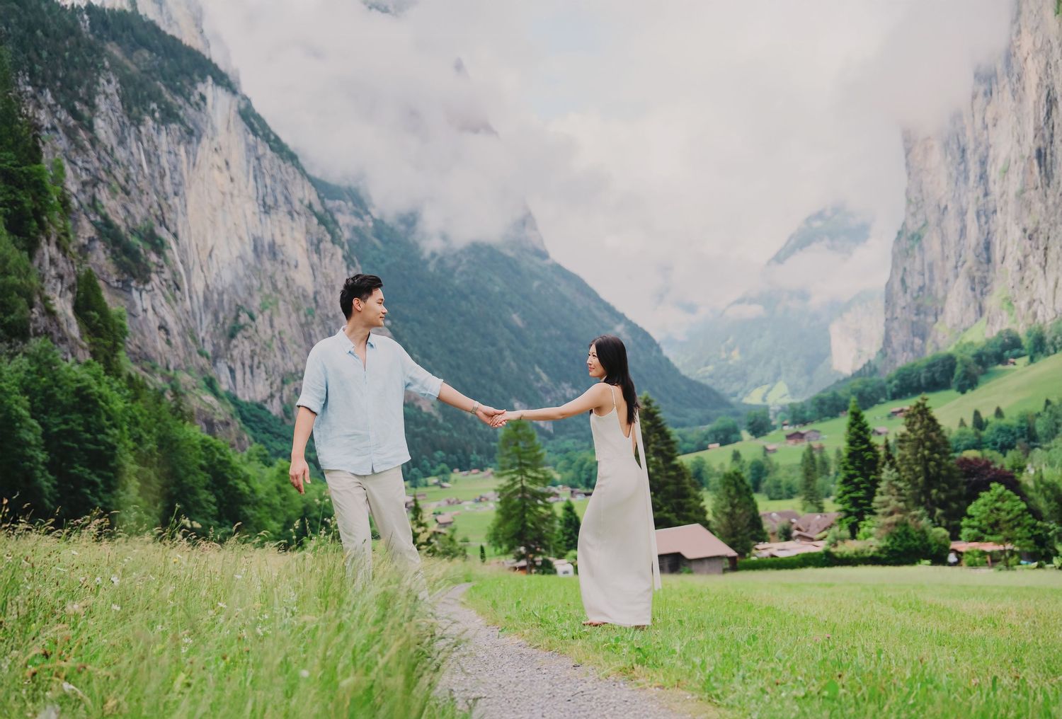 Couple holding hands in a lush green valley with dramatic mountain cliffs in Switzerland.