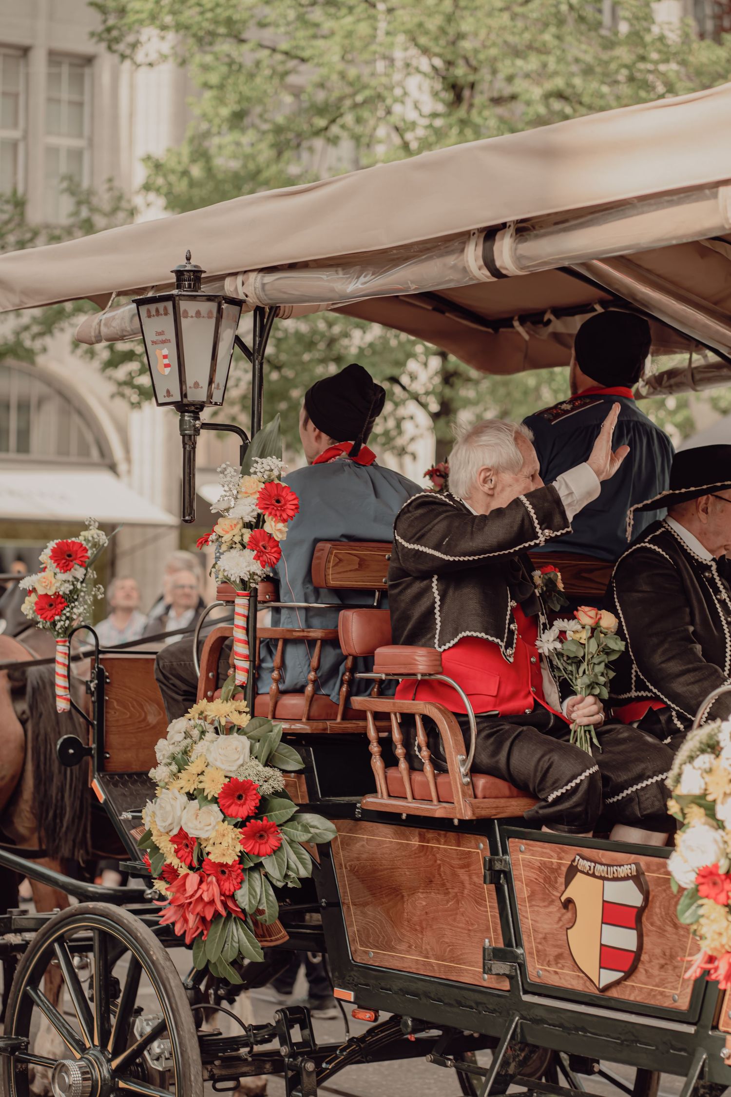 Elaborately dressed participants wave from a flower-adorned vintage carriage during a traditional folk festival parade.
