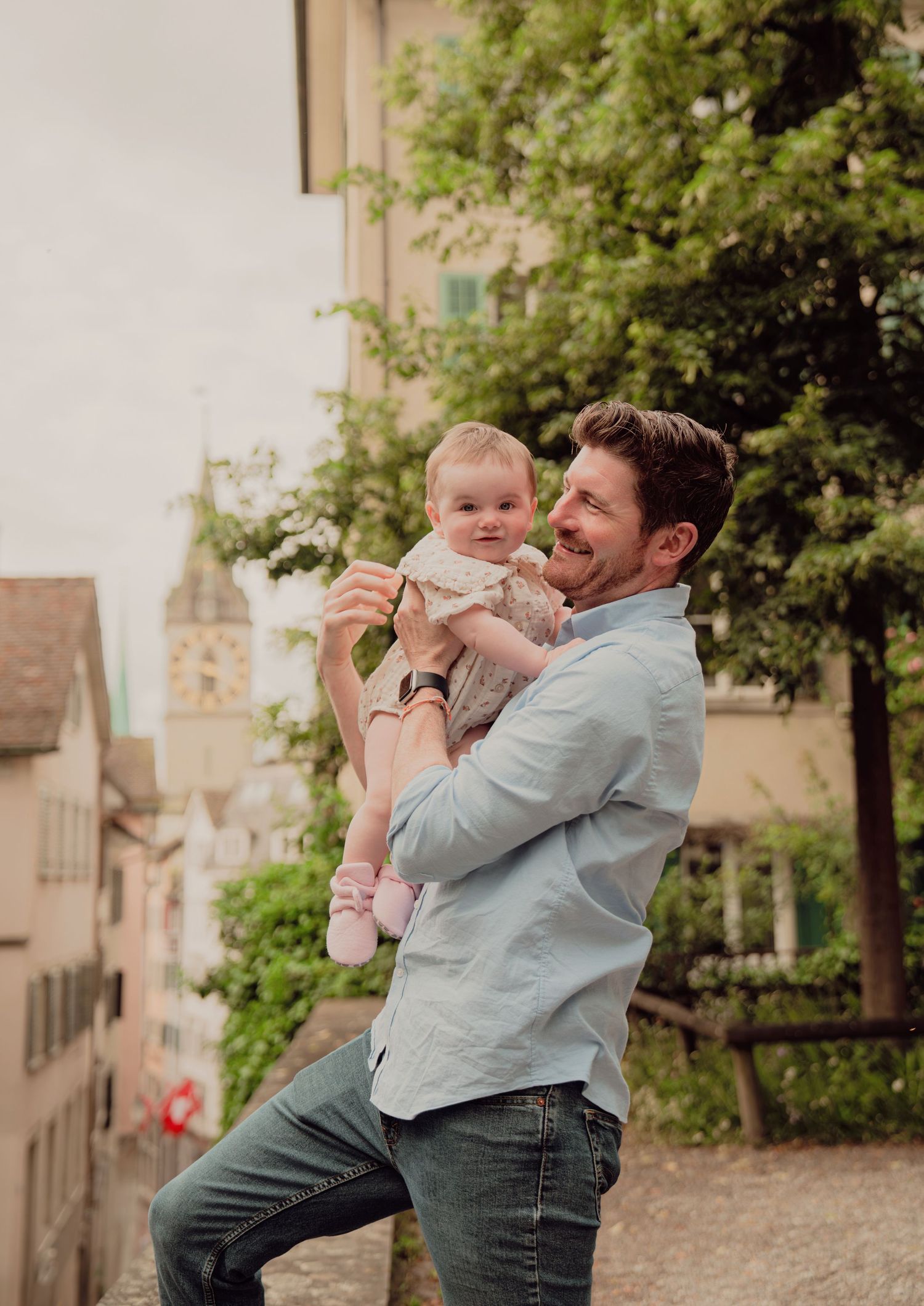Happy father holding baby girl with a historic European town and church tower in background.