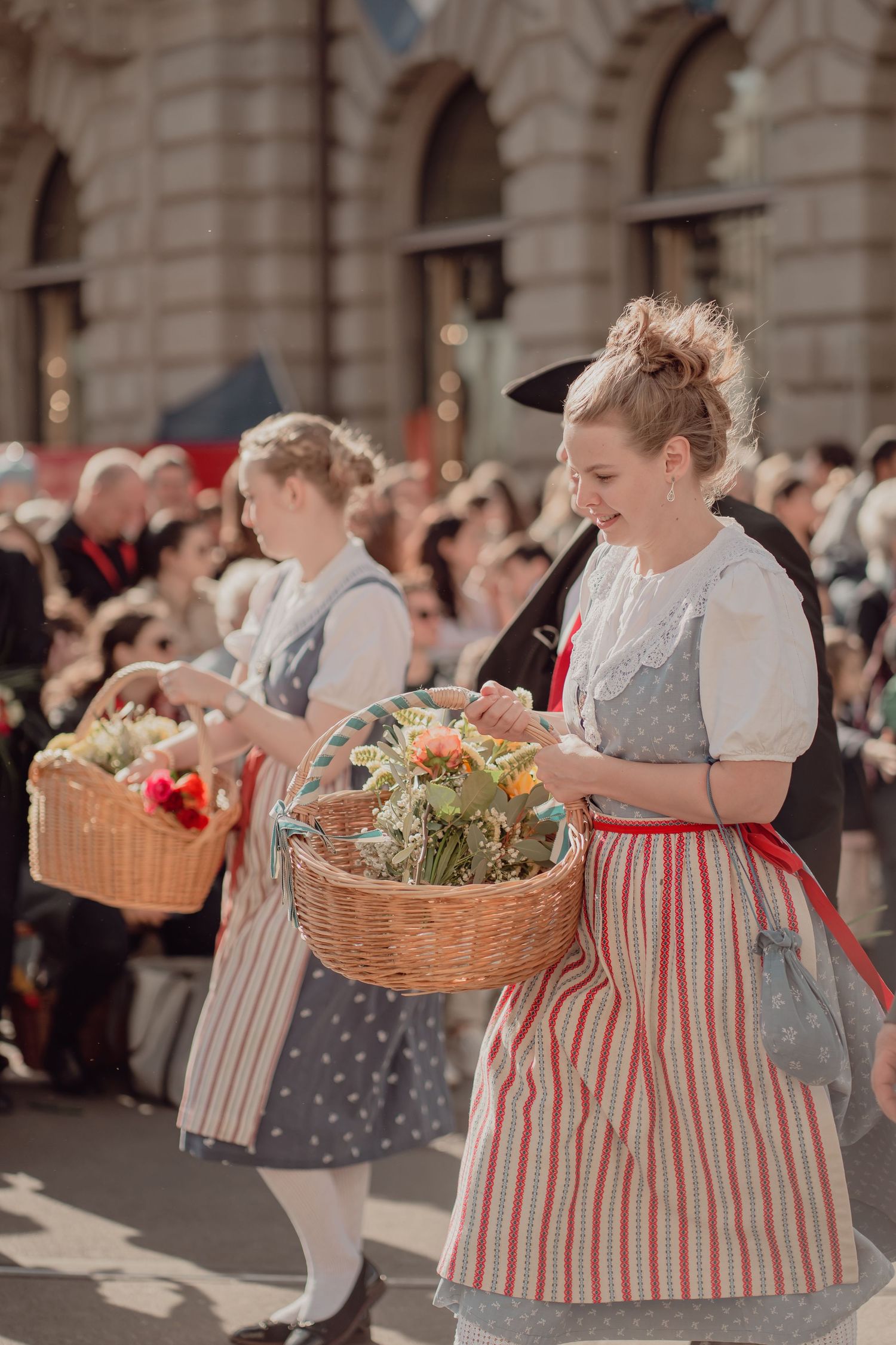 Women in traditional Swiss folk costumes carrying flower-filled wicker baskets at a spring parade.