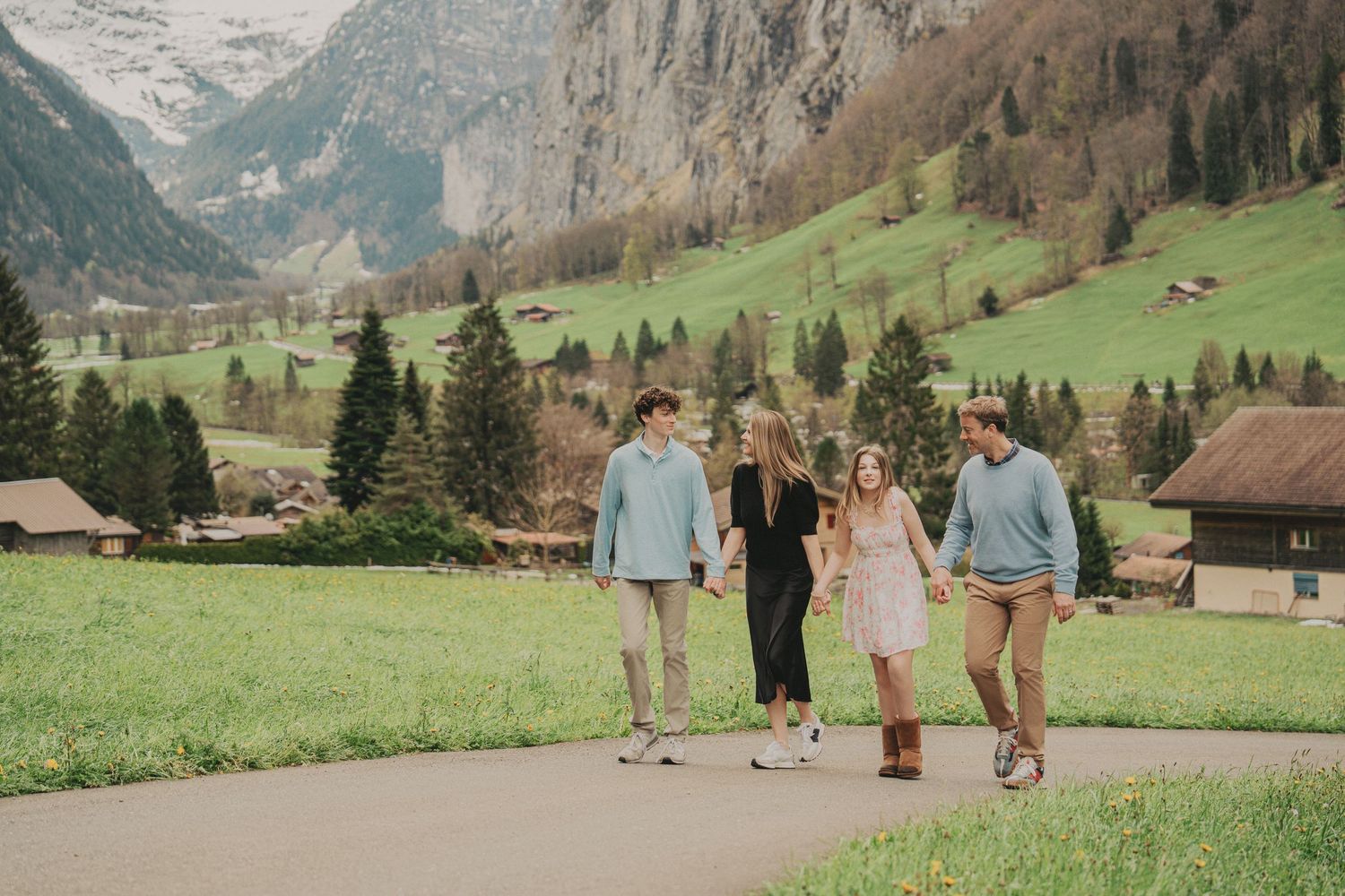 Family of four walking hand in hand on a scenic path in Lauterbrunnen valley, Switzerland.