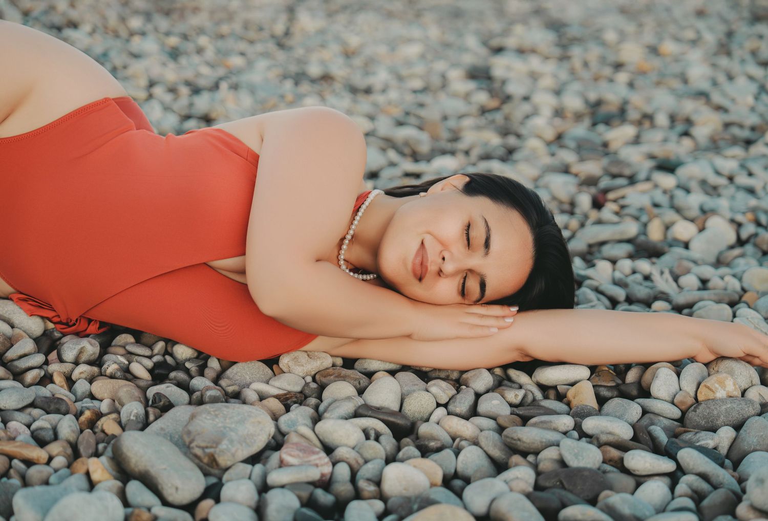 Woman in red swimsuit resting on rocky beach with eyes closed.
