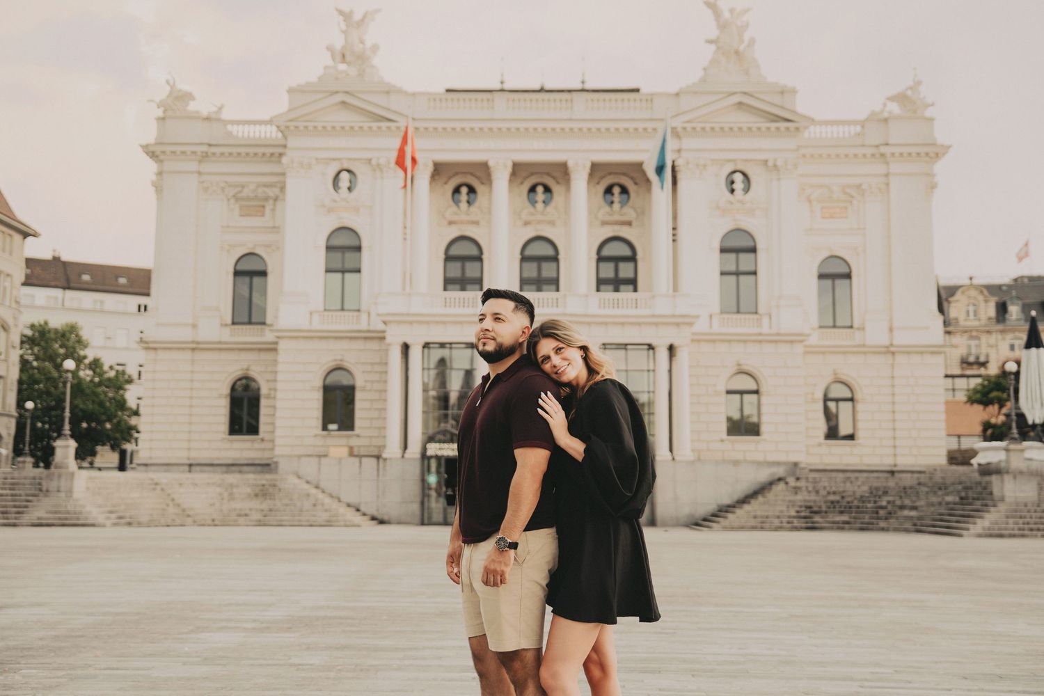 Couple embracing in front of a grand neoclassical European building on an overcast day.